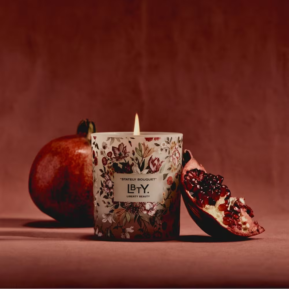 Candle with floral design and 'LBTY' branding next to a pomegranate on a brown background