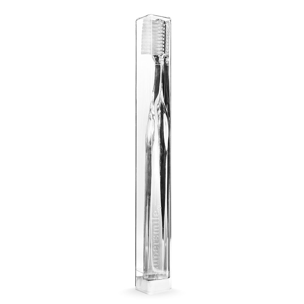 Clear Supersmile toothbrush in a transparent packaging on a white background