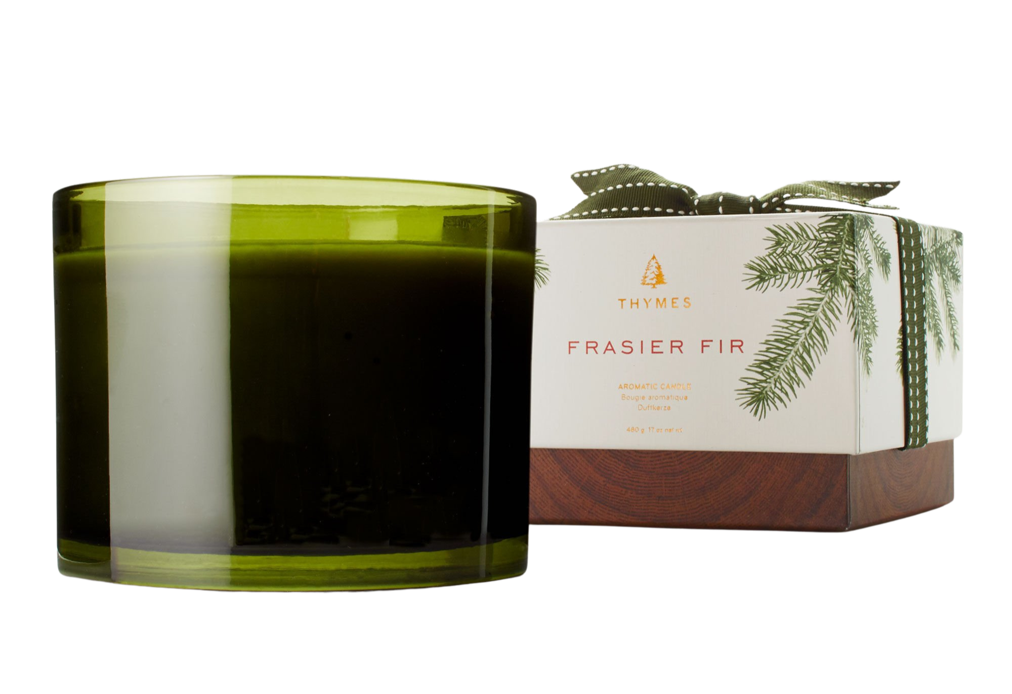 Green candle in a glass container next to its packaging on a white background