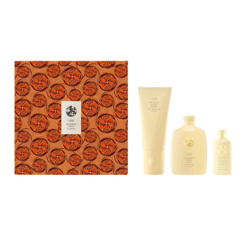 Hair Alchemy Shampoo, Conditioner, Hair Serum alongside orange print packaging on a white backdrop 