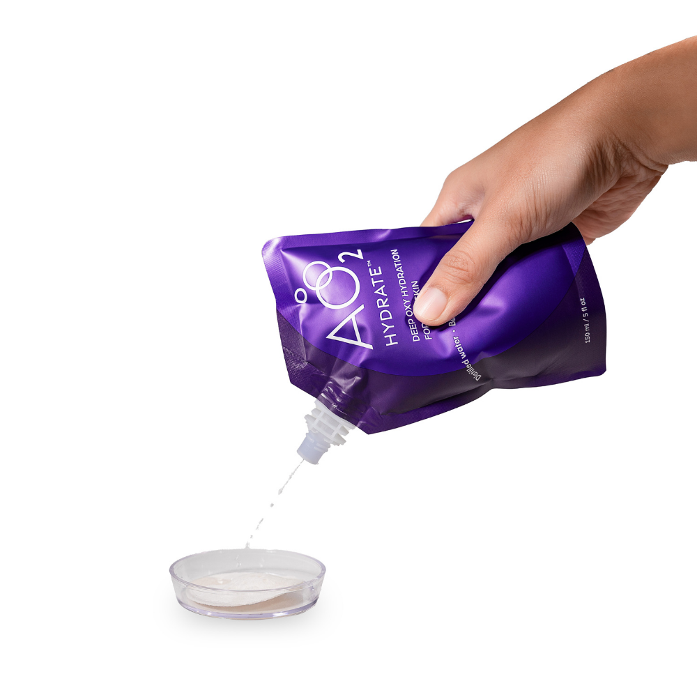 Hand pouring products  from a purple A02 Hydrate packet into a small container on a white background.