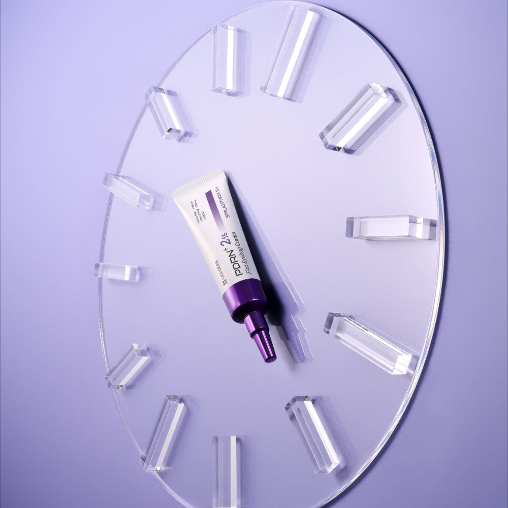 A cosmetic tube with a purple cap and white body, placed on a clear circular acrylic clock against a light lavender background.