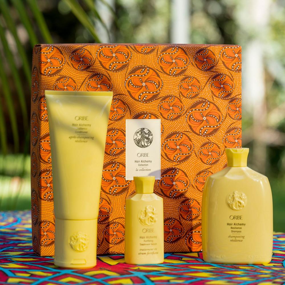 Hair Alchemy Shampoo, conditioner, hair serum treatment with orange gift box packaging on a green outdoor landscape 