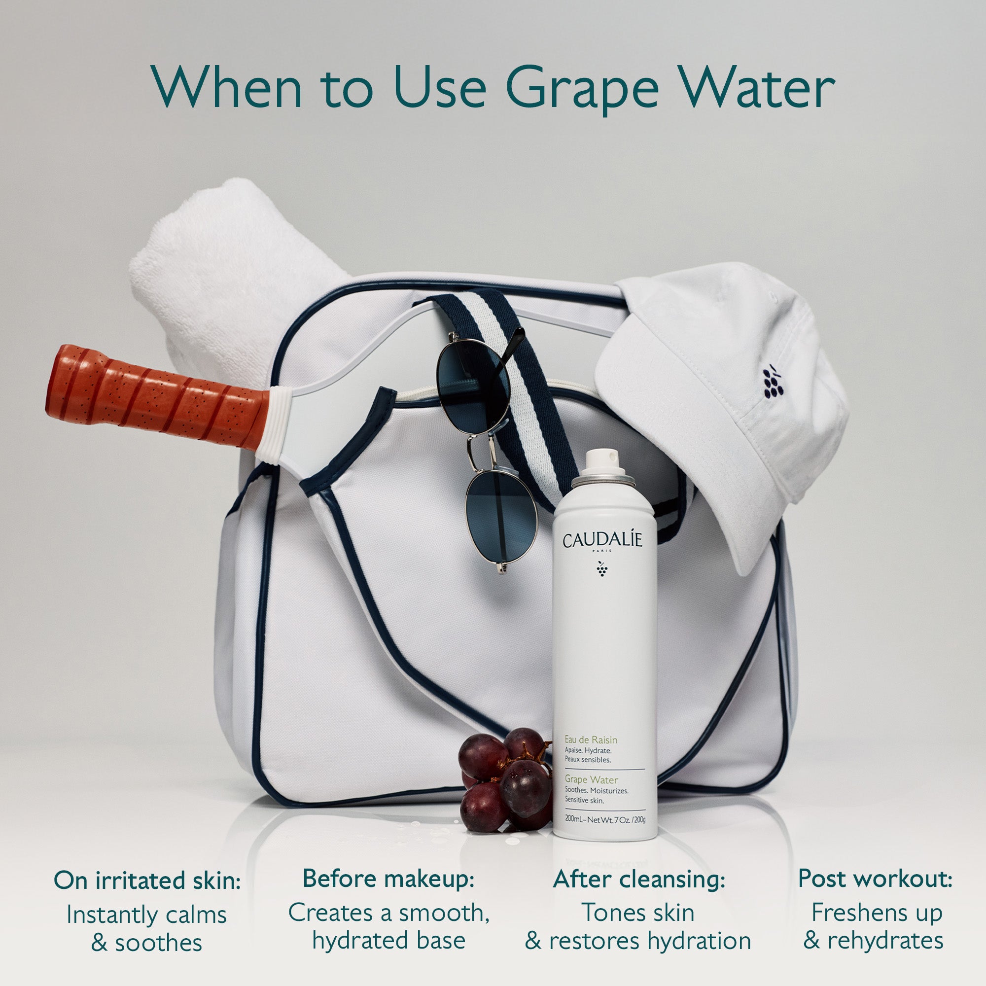 Caudalie grape water bottle with a white bag, grapes, and a paddle on a light gray background.