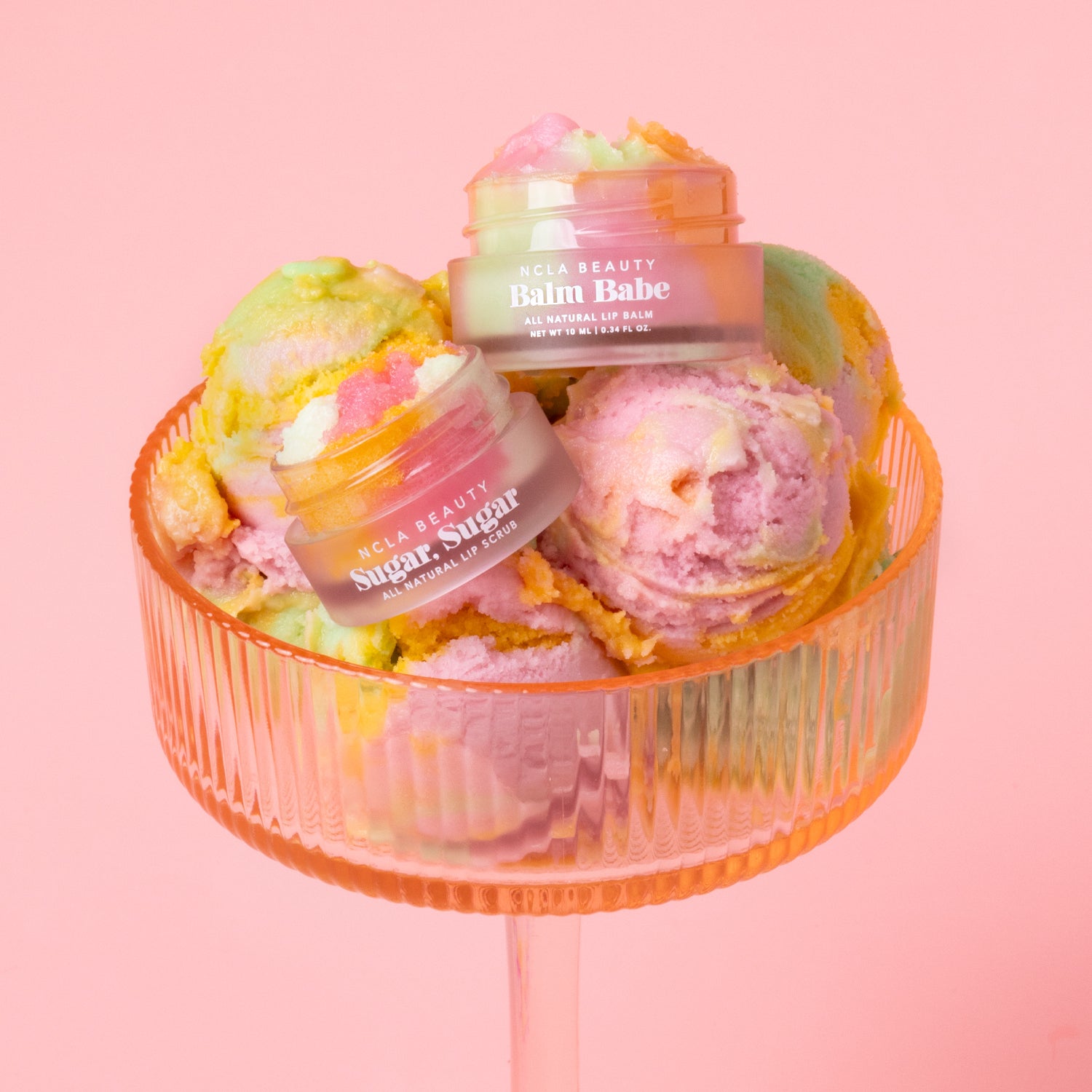 Lip balm and lip scrub containers with colorful balm in a transparent orange holder on a pink background