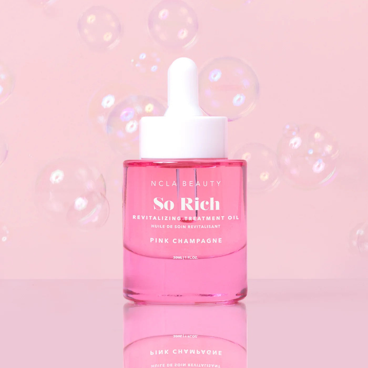 Pink bottle of NCLA Beauty So Rich Revitalizing Treatment Oil on a pink background with bubbles.