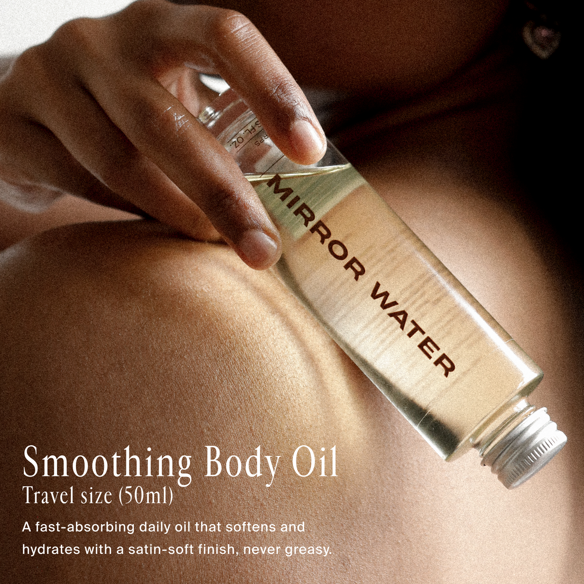 A hand holds a small clear bottle labeled 'MIRROR WATER' body oil against a person's bare chest. Text on the image reads 'Smoothing Body Oil' and 'Travel size (50ml)'.
