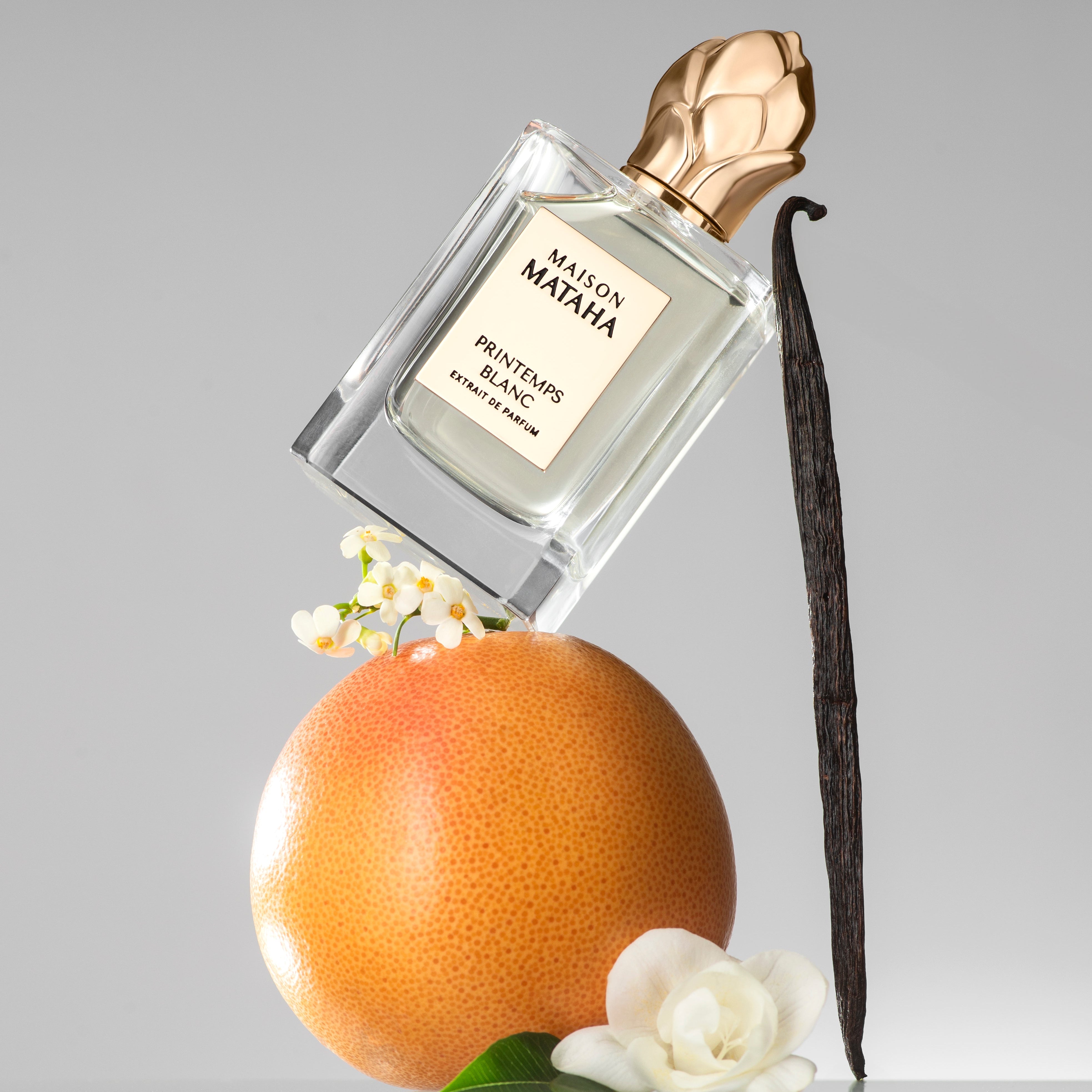 Perfume bottle leaning on a vanilla bean pod and an orange