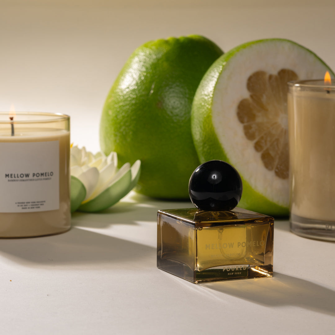 Perfume bottle labeled 'Mellow Pomelo' with candles and fruit on a light background