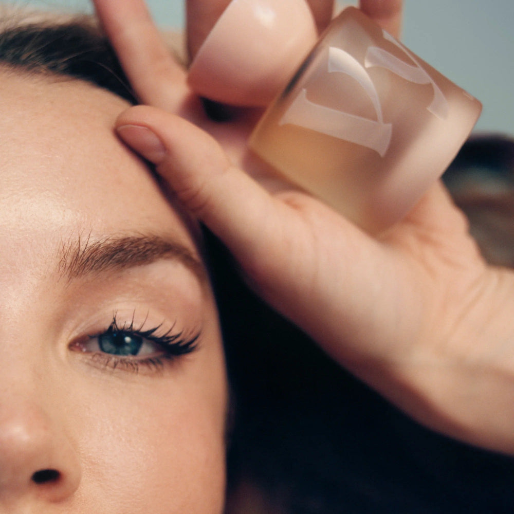 Close-up of a woman's face with a hand holding a bottle of Ludeaux eau de parfum near her eye.