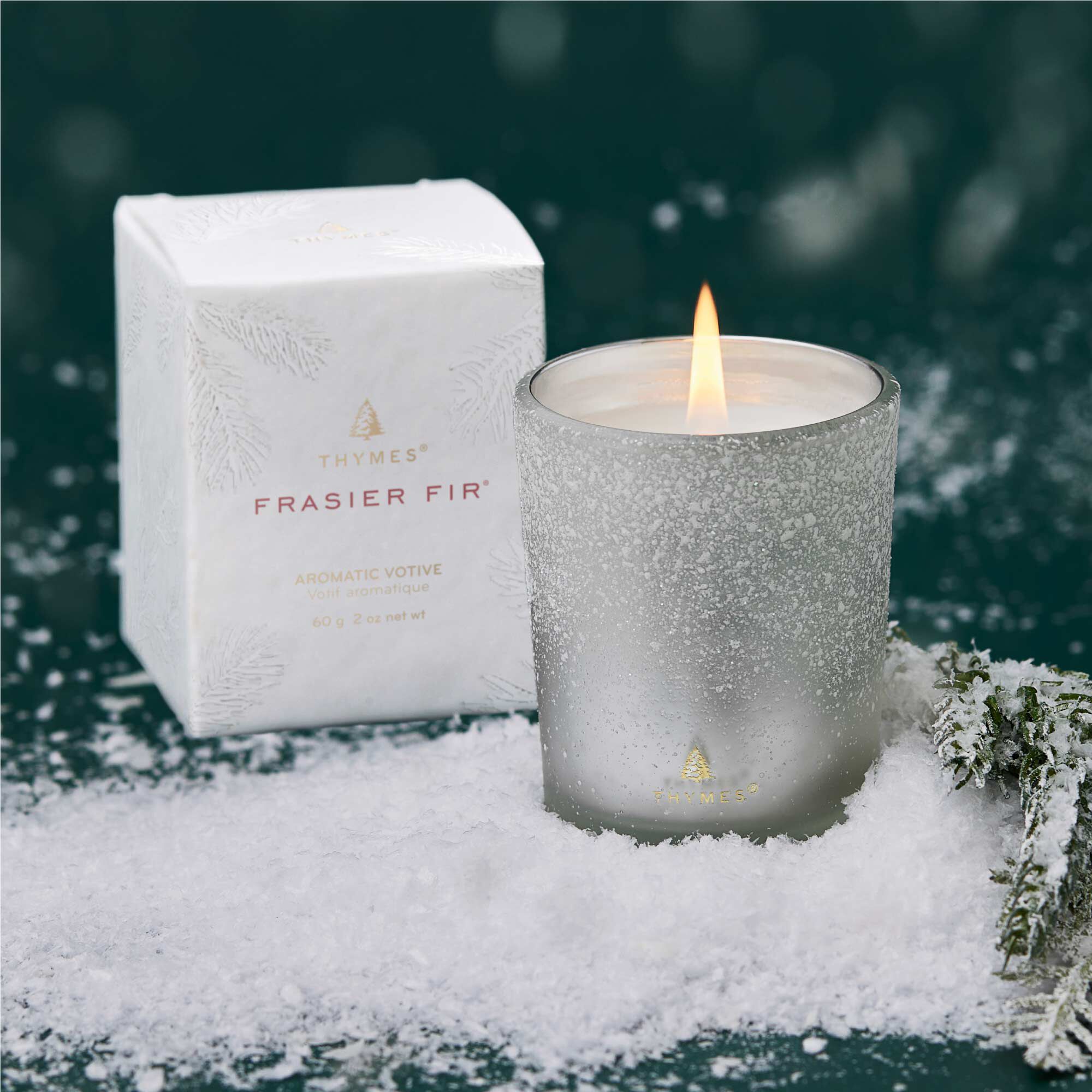 Thymes Frasier Fir candle in a snowy setting with packaging