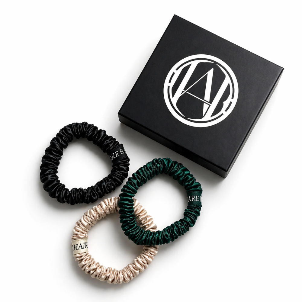 Three hair scrunchies in black, green, and beige with a branded box on a white background.