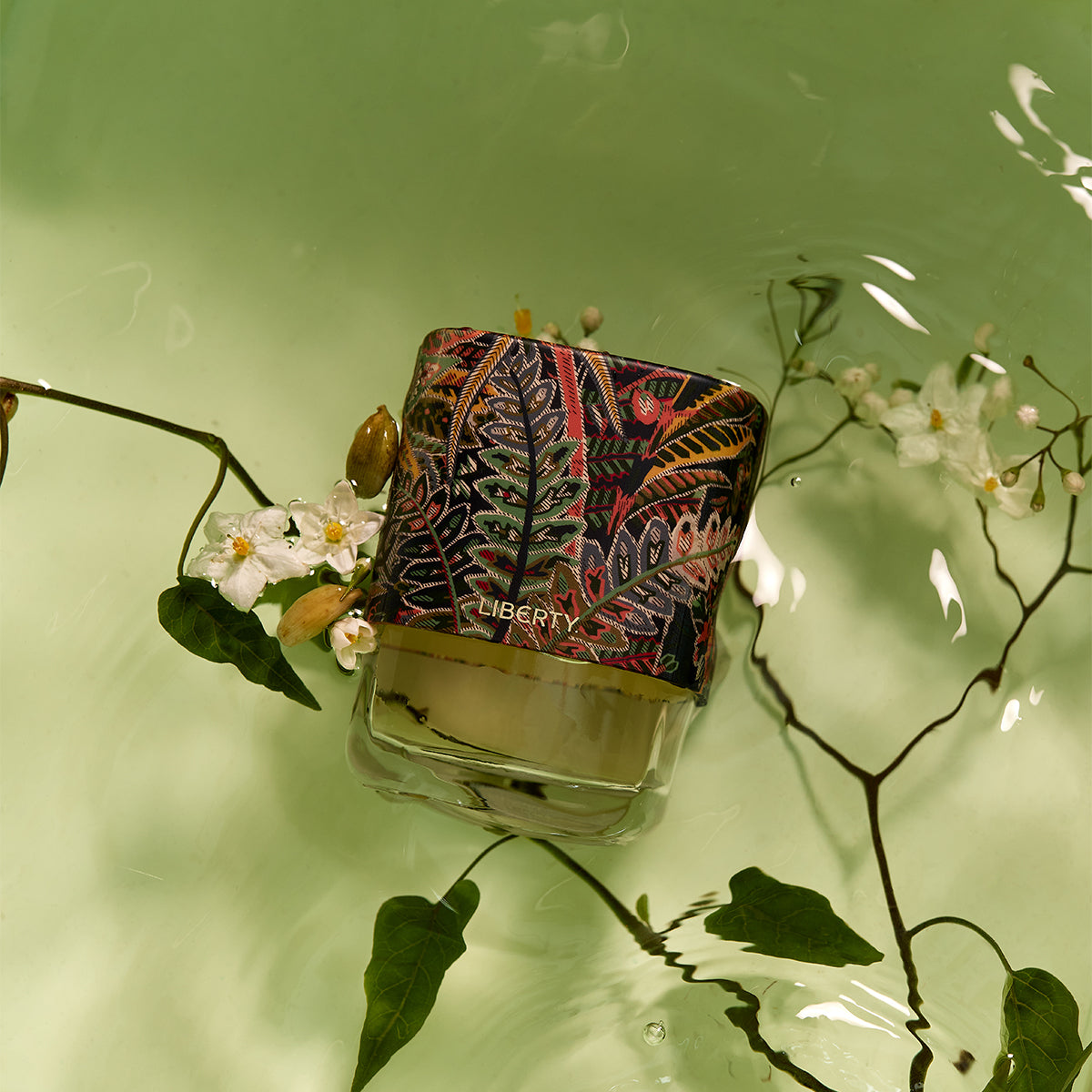 Perfume bottle with decorative label floating on water surrounded by plants and flowers