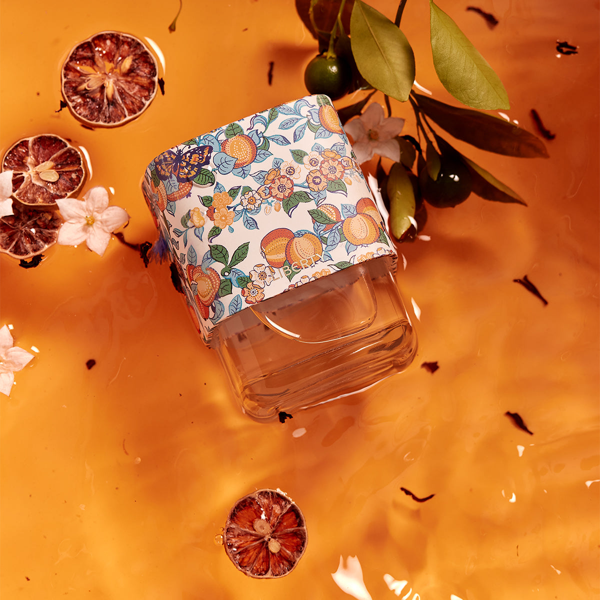 Perfume bottle with floral patterned cap on an orange background with dried fruits and flowers
