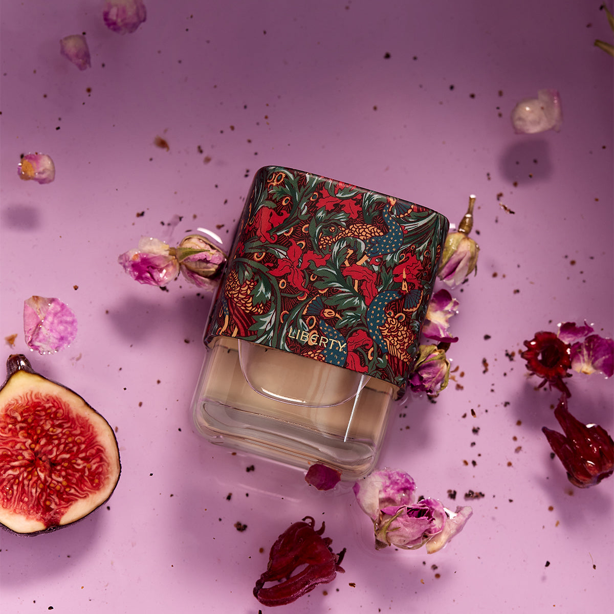 Perfume bottle with floral design packaging on a pink background with flowers and figs.