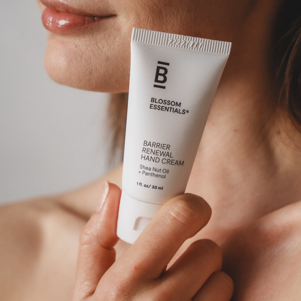 Person holding a tube of Blossom Essentials Barrier Renewal Hand Cream close to their face.