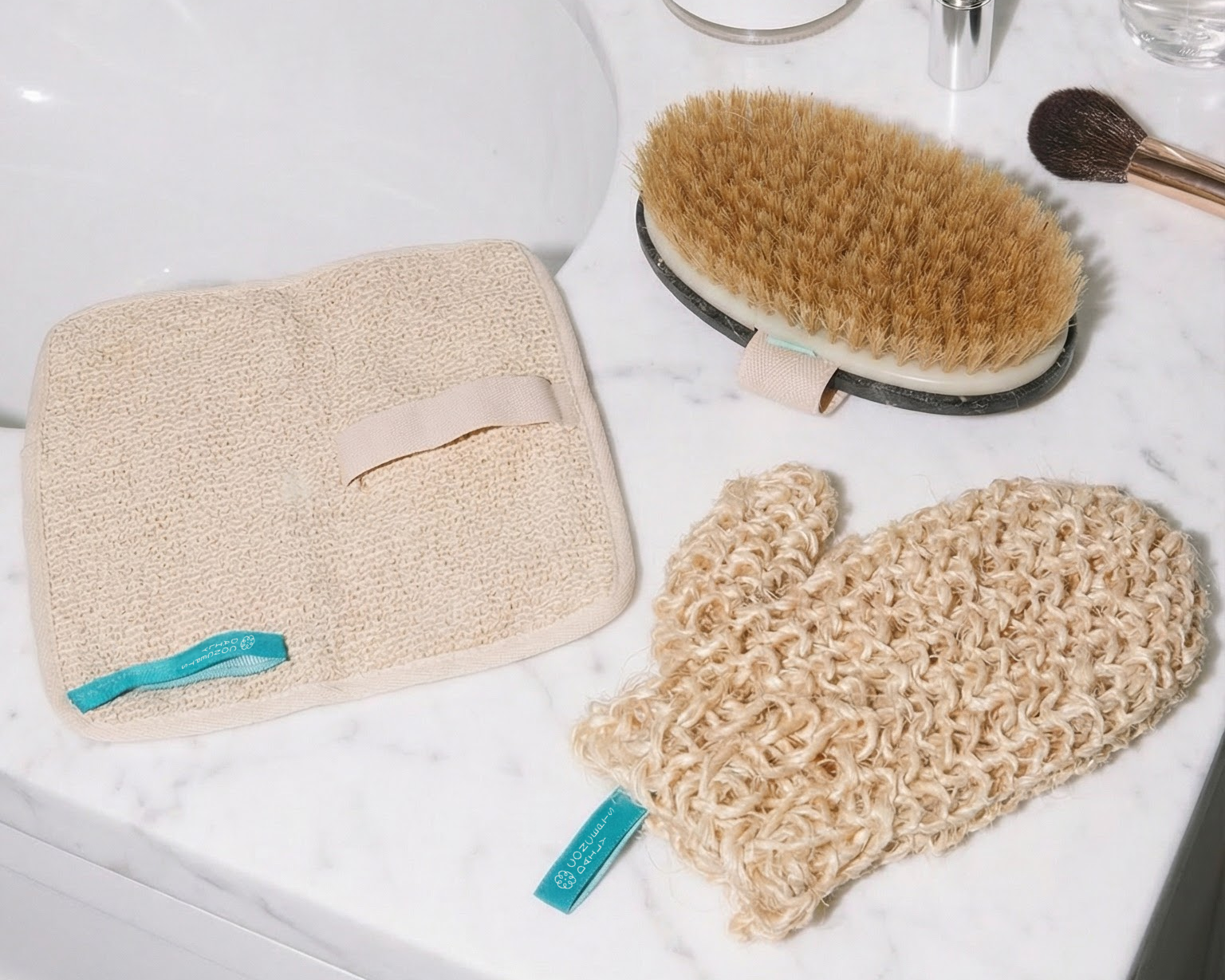 Bathroom counter with various skincare and beauty products including a brush, mitt, and towels.