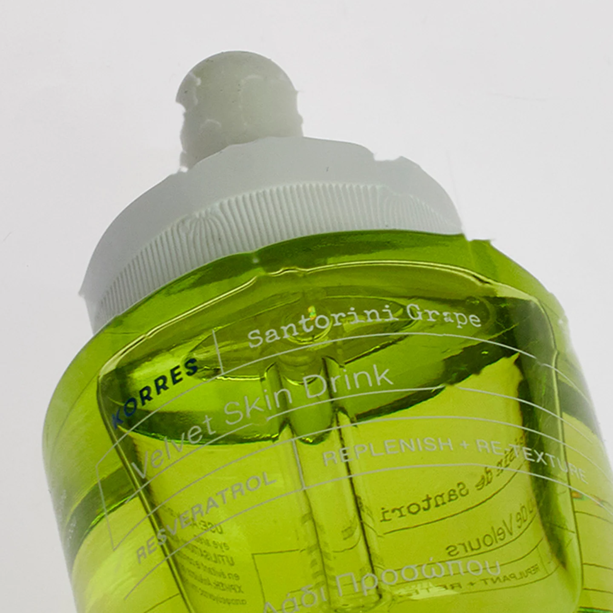 Clear bottle with green liquid and white cap on a light gray background