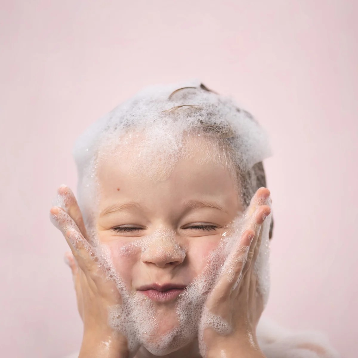 Child with soap suds on a pink background