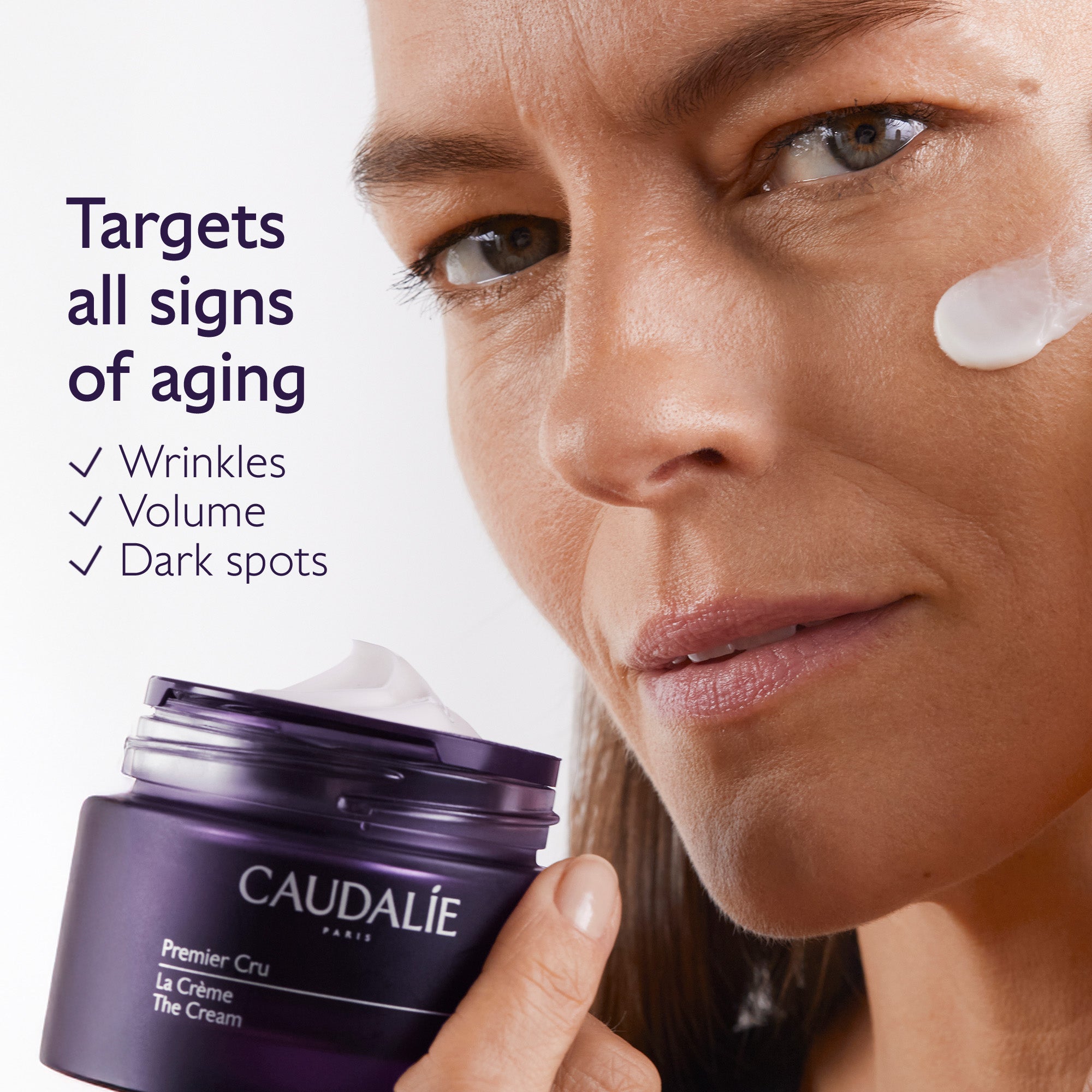 Woman applying cream to her face with a Caudélie jar in the foreground, highlighting anti-aging benefits.
