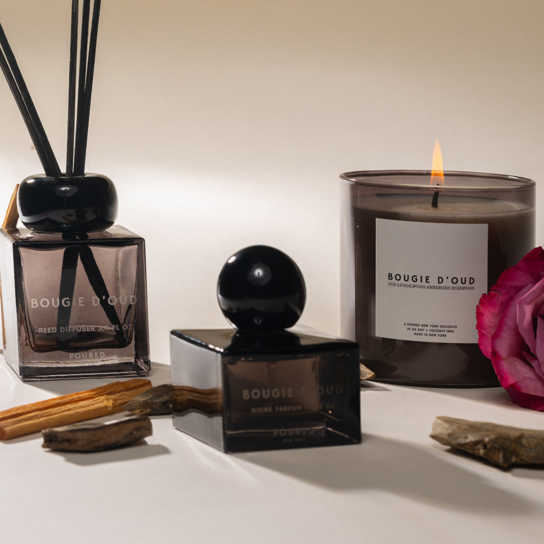 Bougie d'Oud candles and diffuser on a white surface with a pink flower.