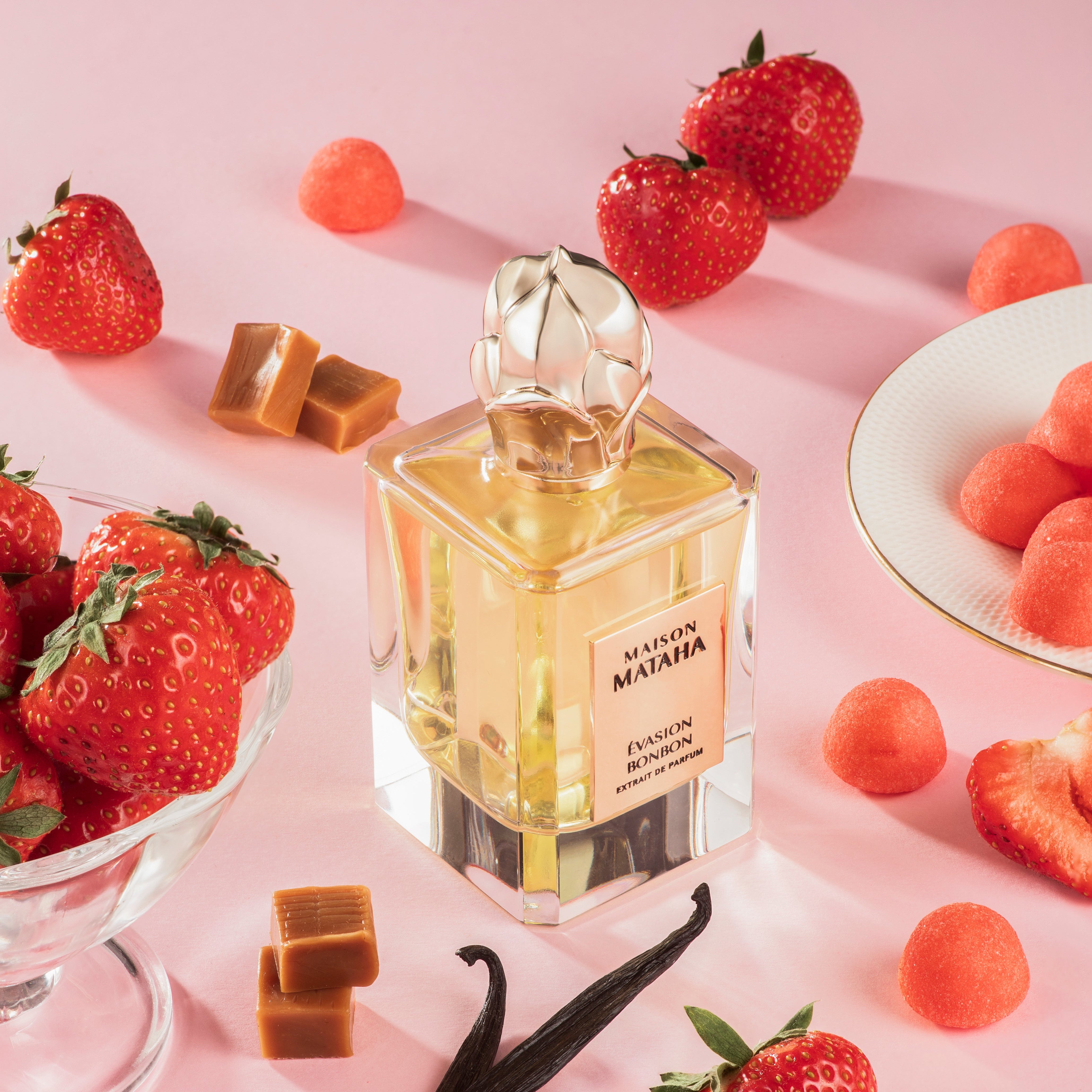 Maison Mataha perfume bottle surrounded by strawberries, vanilla and caramel on a pink background