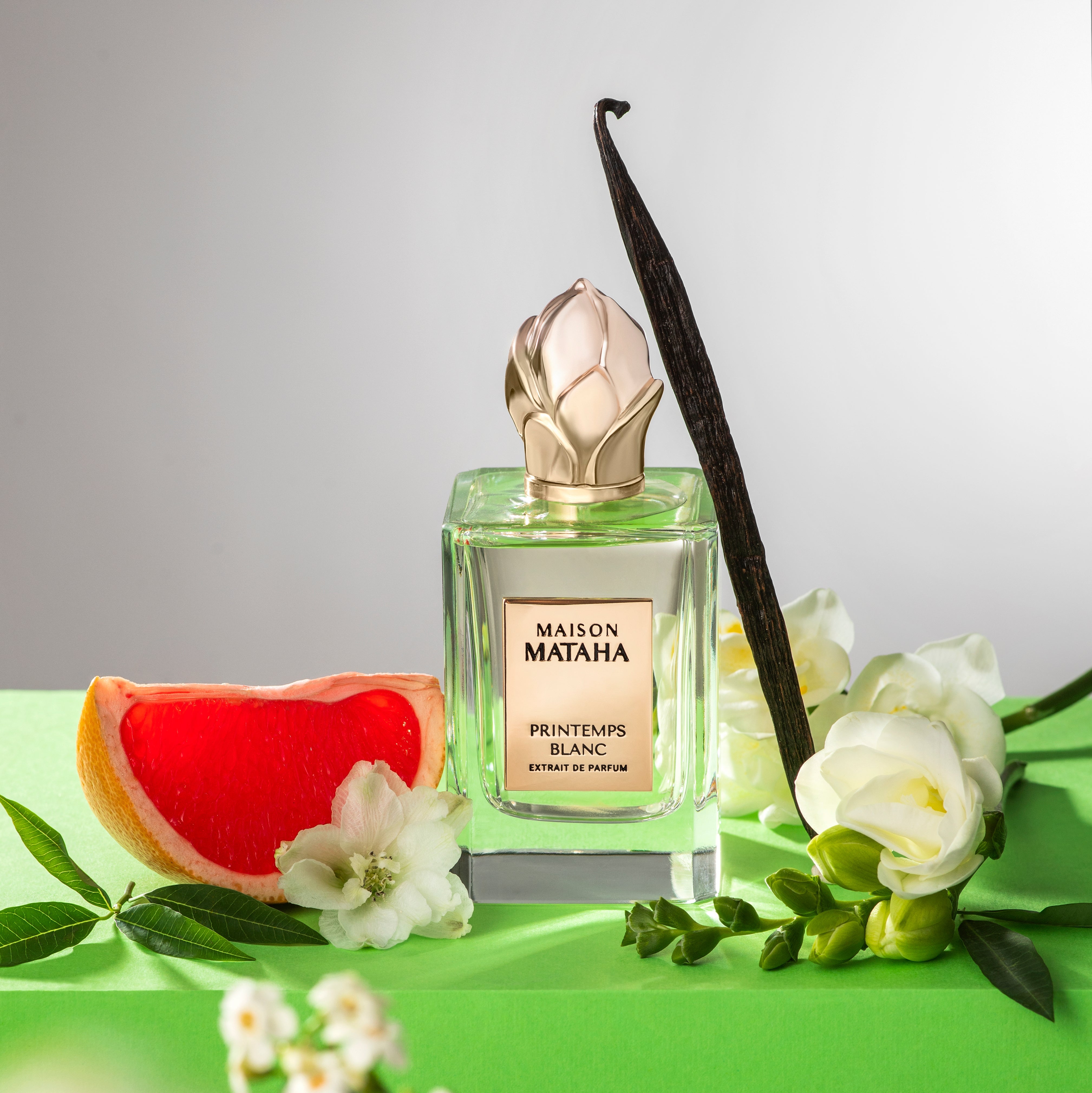 Perfume bottle next to vanilla, flowers, and citrus fruit