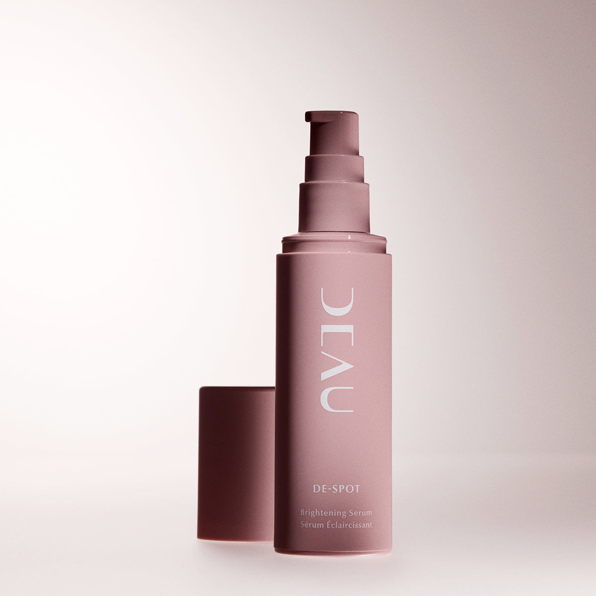 Skincare serum bottle with pump on a light pink background
