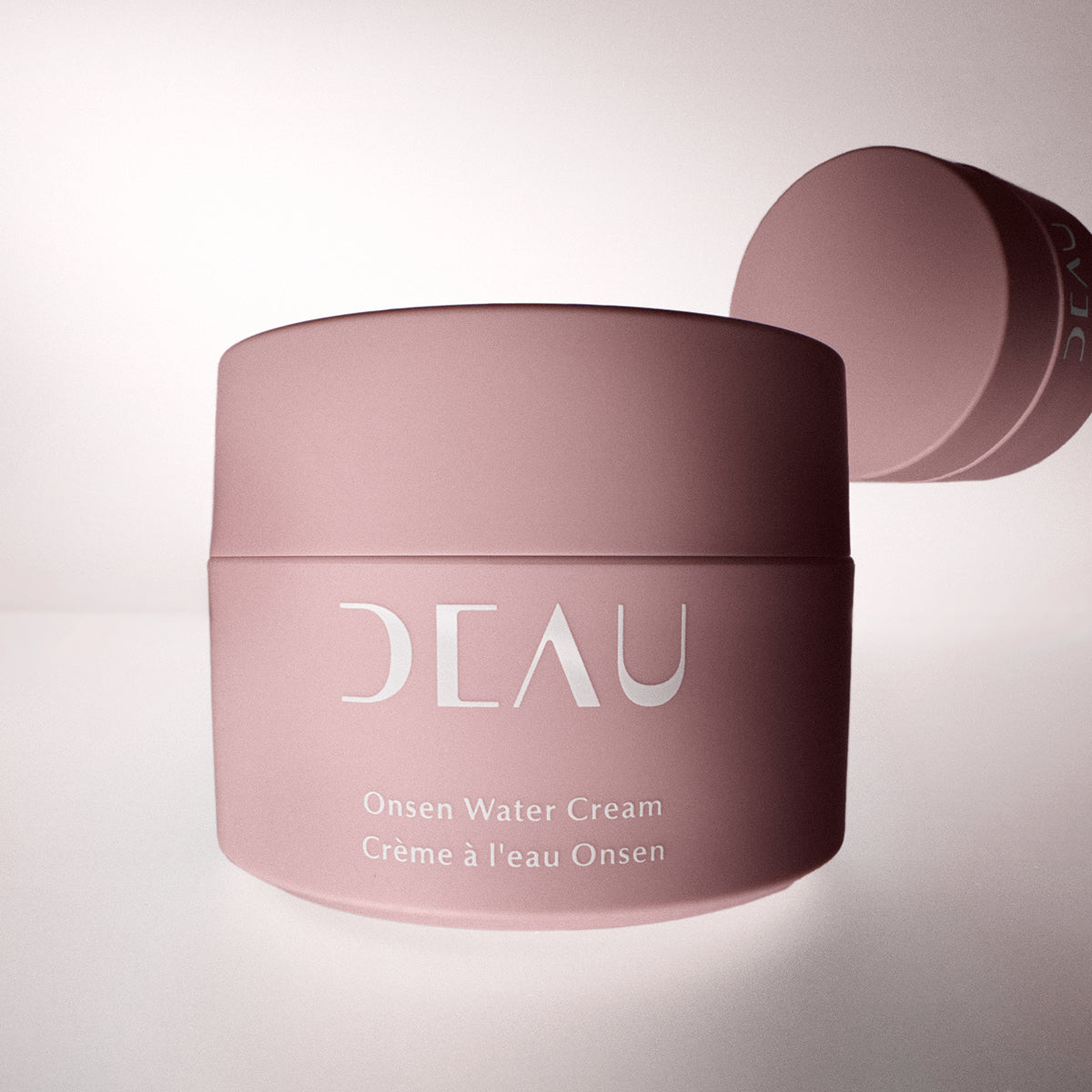 Pink jar of DEAU Onsen Water Cream on a light pink background