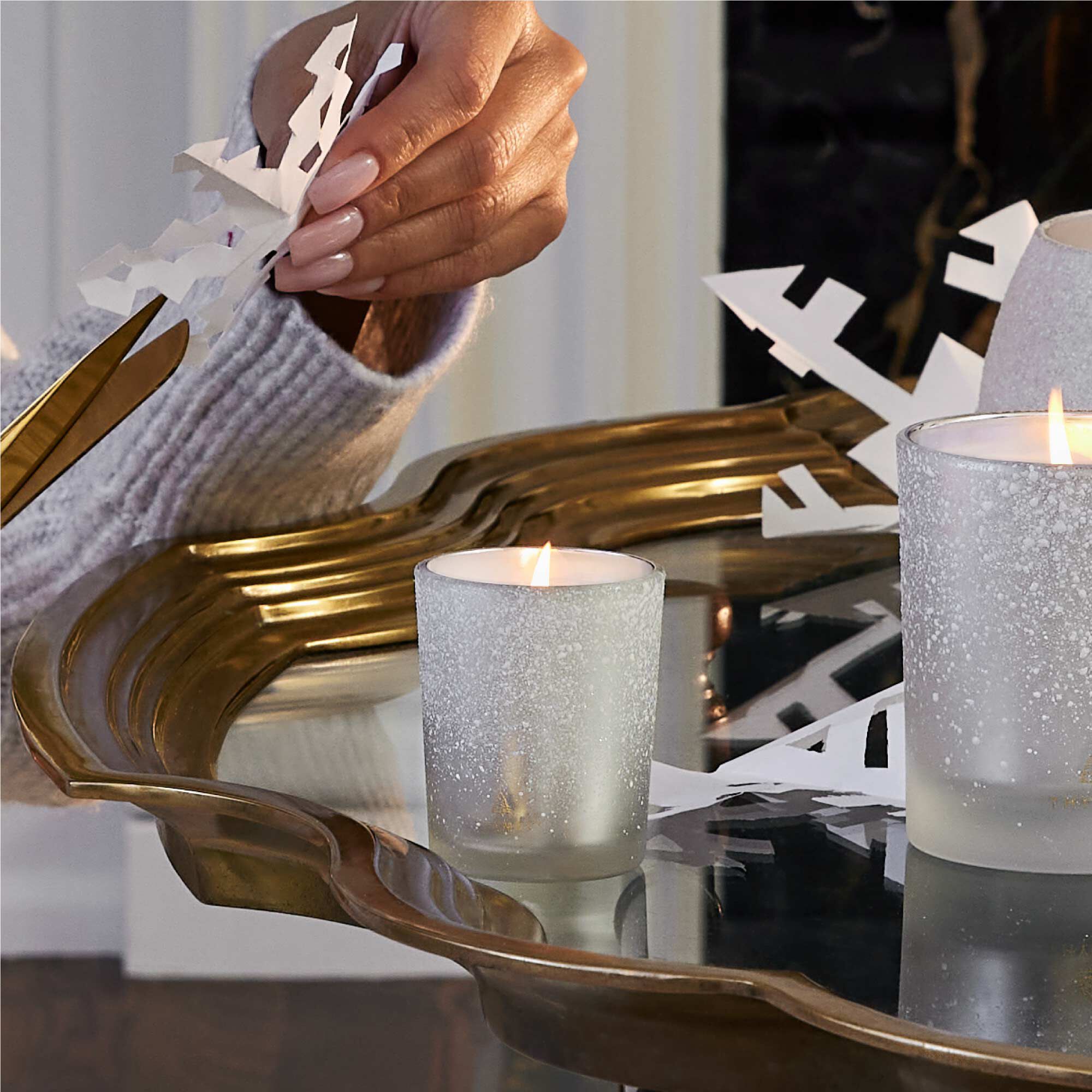Person holding a paper snowflake near two lit candles on a decorative tray.