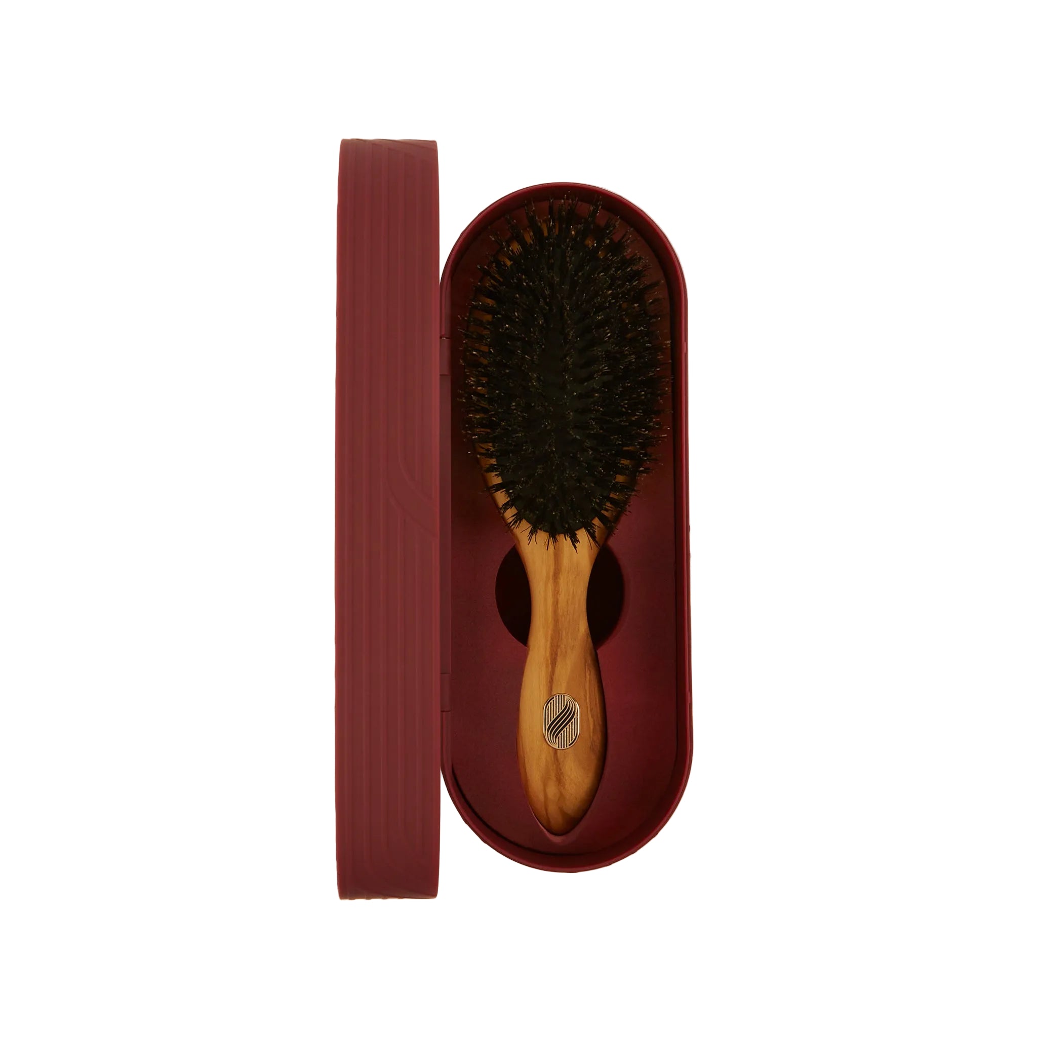 A wooden hairbrush with dark bristles sits inside an oval burgundy case next to its matching lid, photographed on a clean off-white background.
