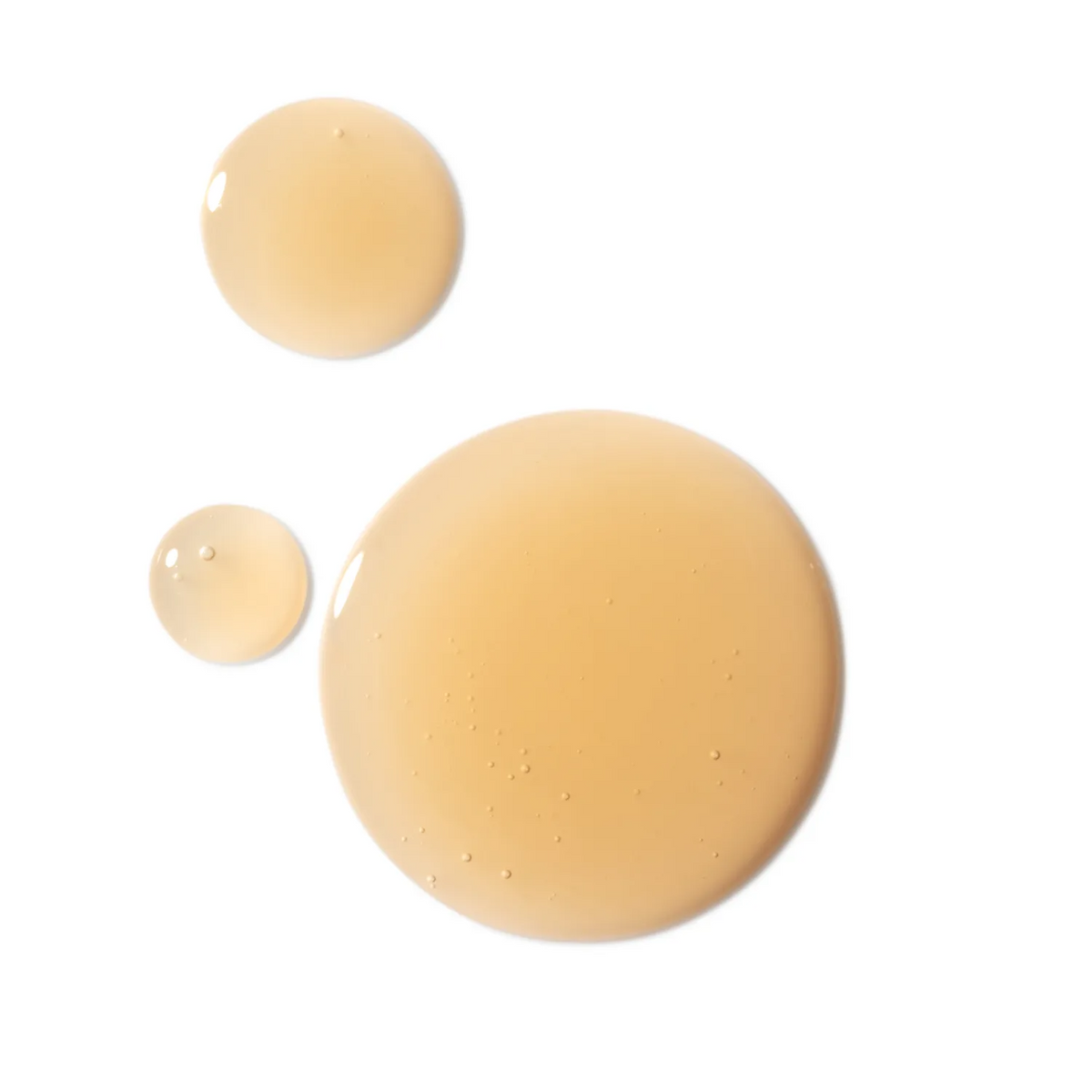 Three translucent droplets of a light peach-beige cosmetic gel or serum on a solid white background, showcasing a glossy, semi-opaque texture.