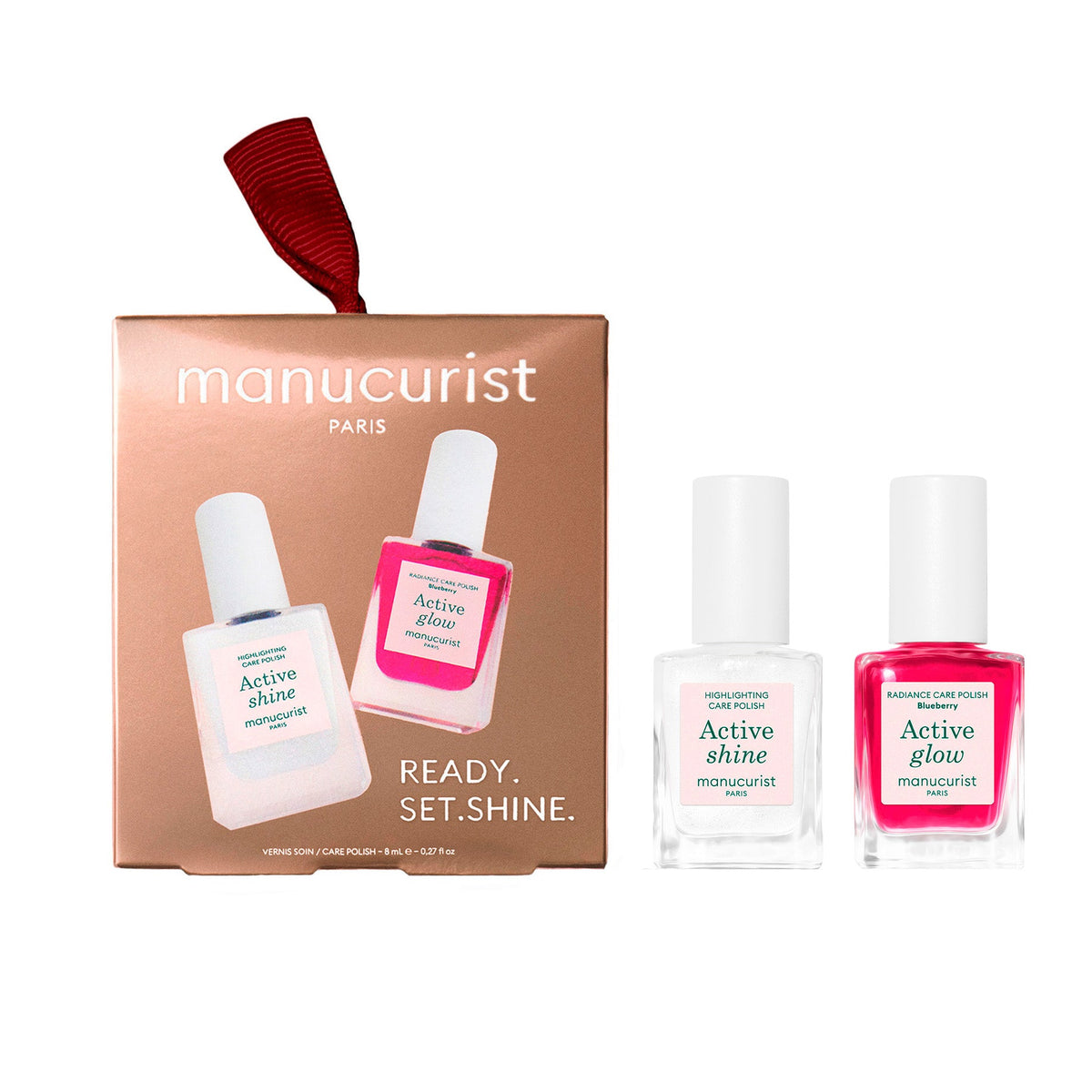 Manucurist Paris nail polish gift set featuring a rose gold box with a red ribbon, alongside two bottles of nail polish: one in clear liquid with a white cap and label, and one in bright pink liquid with a white cap and label.