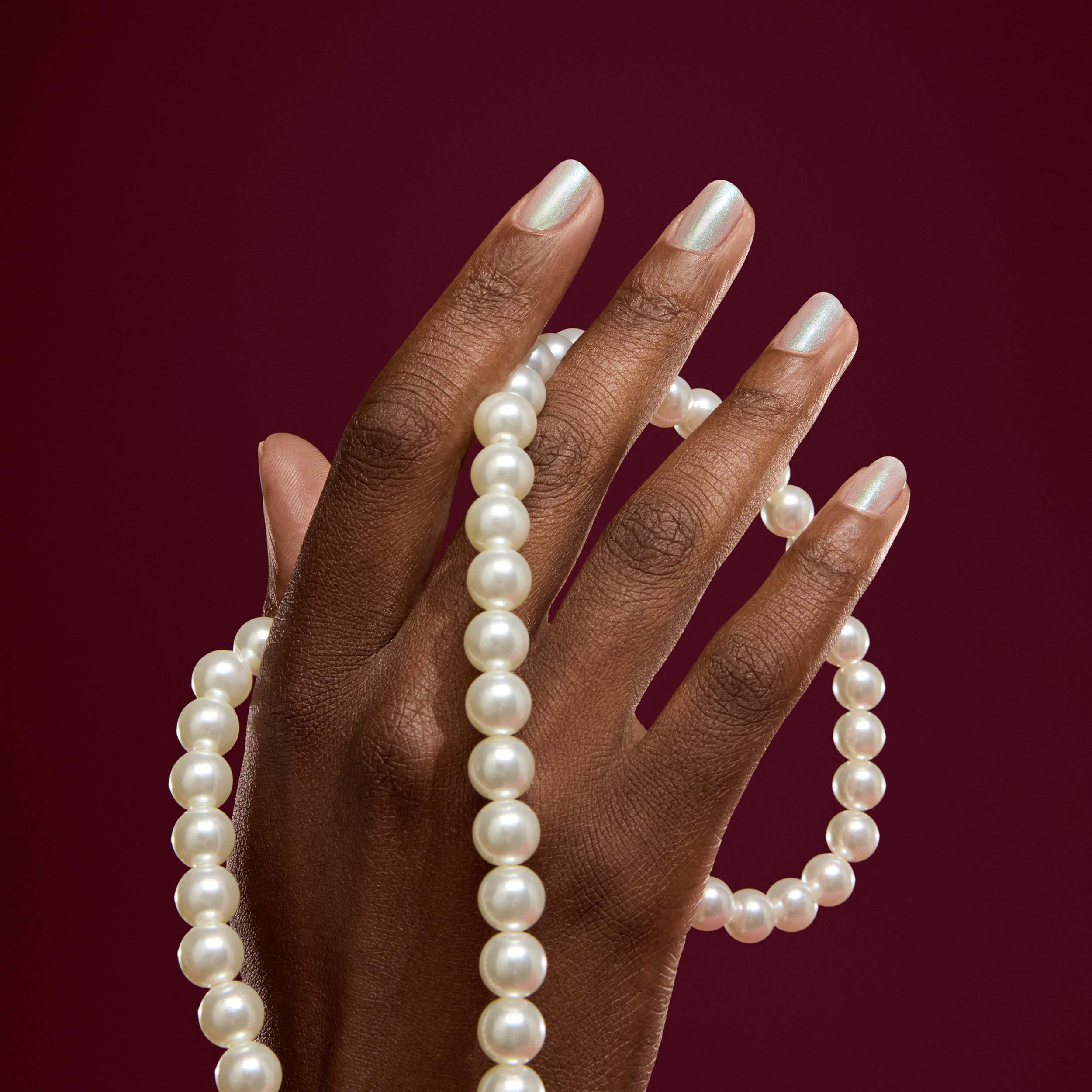 Hand holding a pearl necklace against a red background
