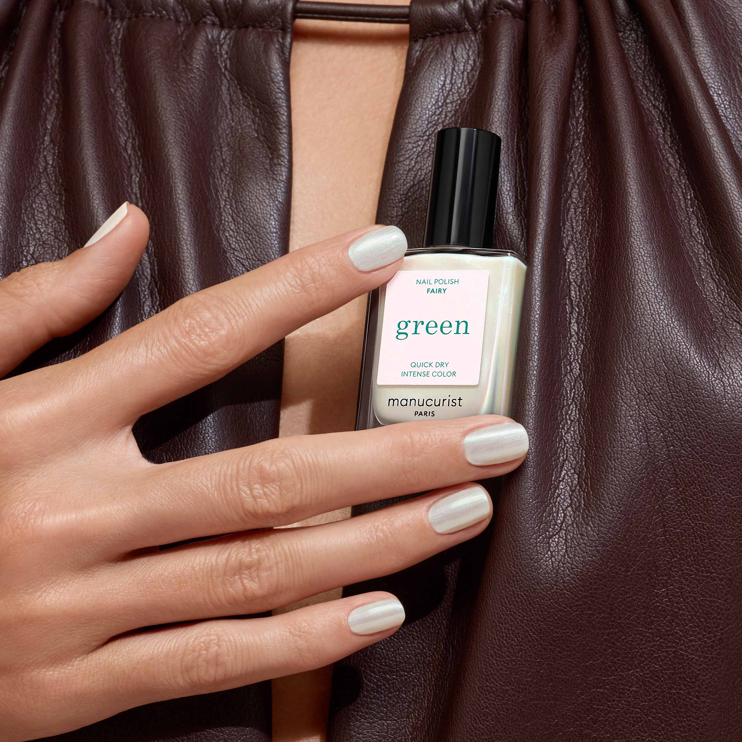Hand holding a bottle of Fairy nail polish against a brown leather background