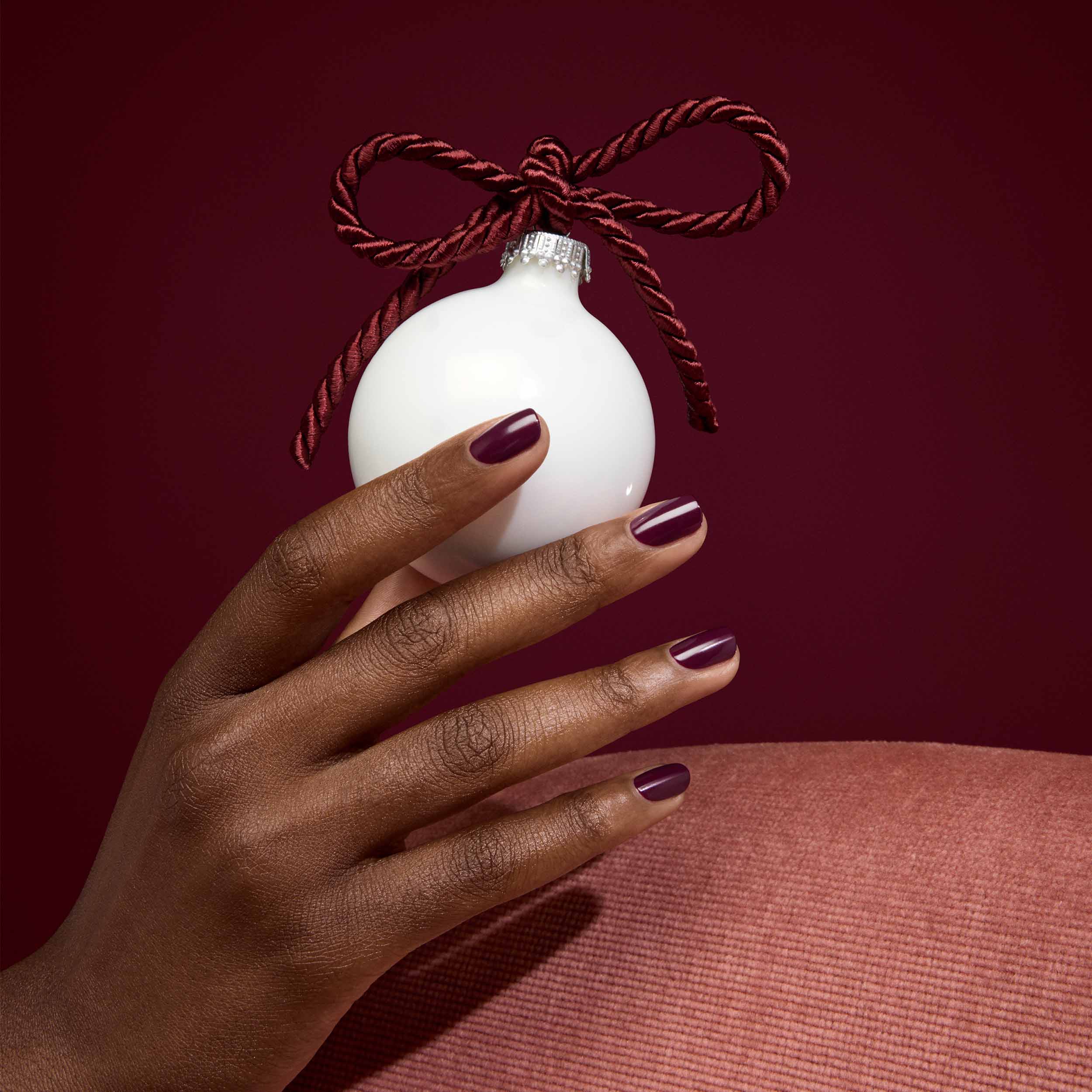 Hand holding a white ornament with a brown ribbon against a red background