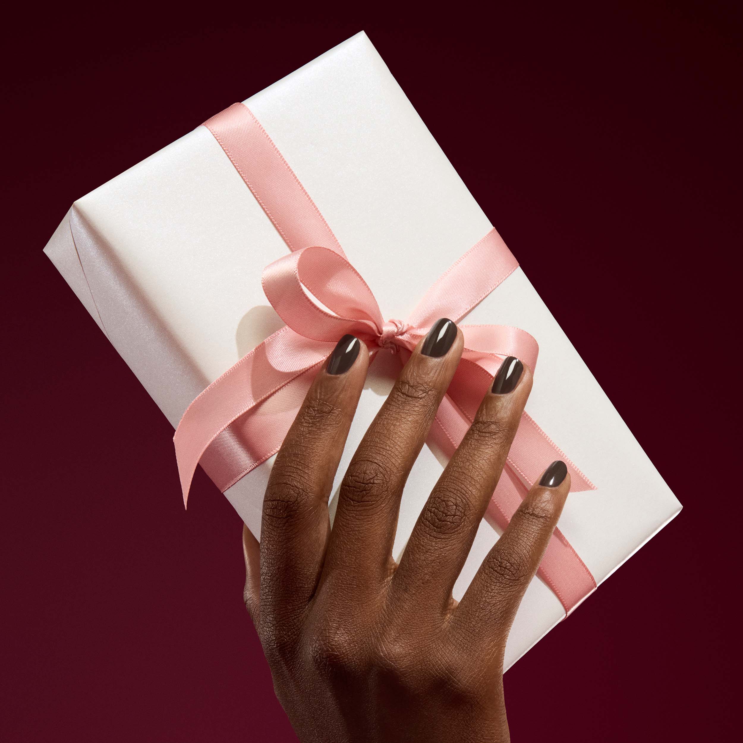 Hand holding a white gift box with a pink ribbon against a dark background