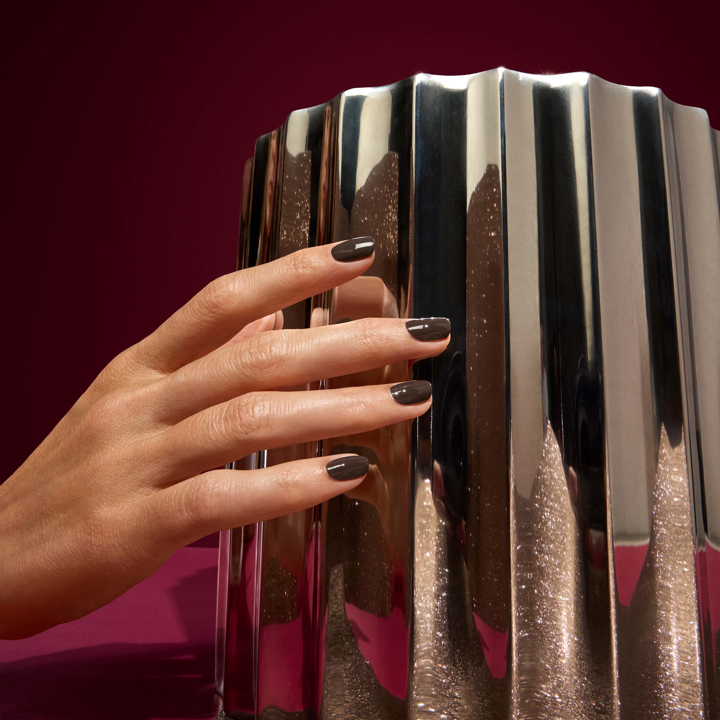 Hand with dark nail polish touching a metallic, ribbed surface against a red background
