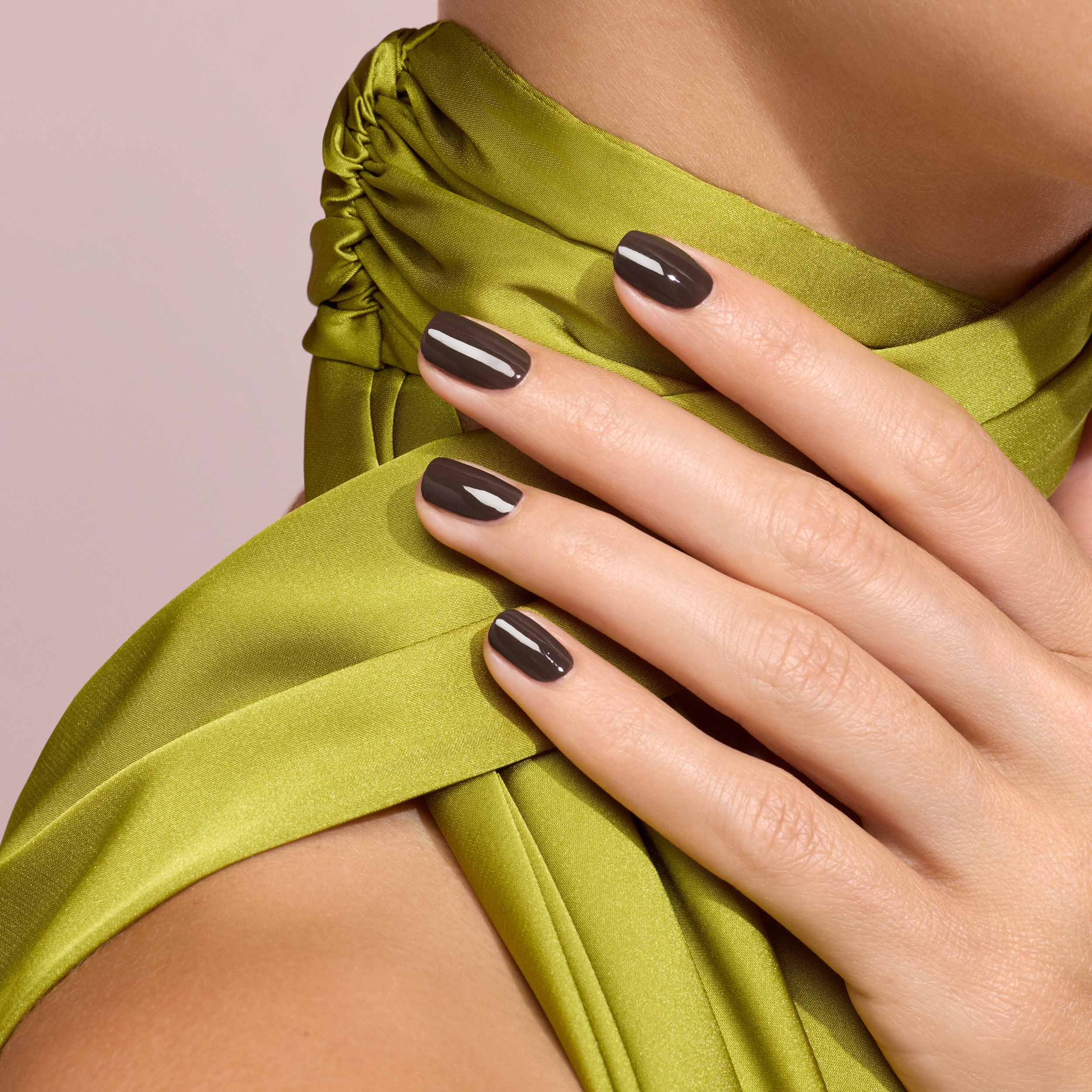 Close-up of a hand with dark nail polish on a green garment against a pink background