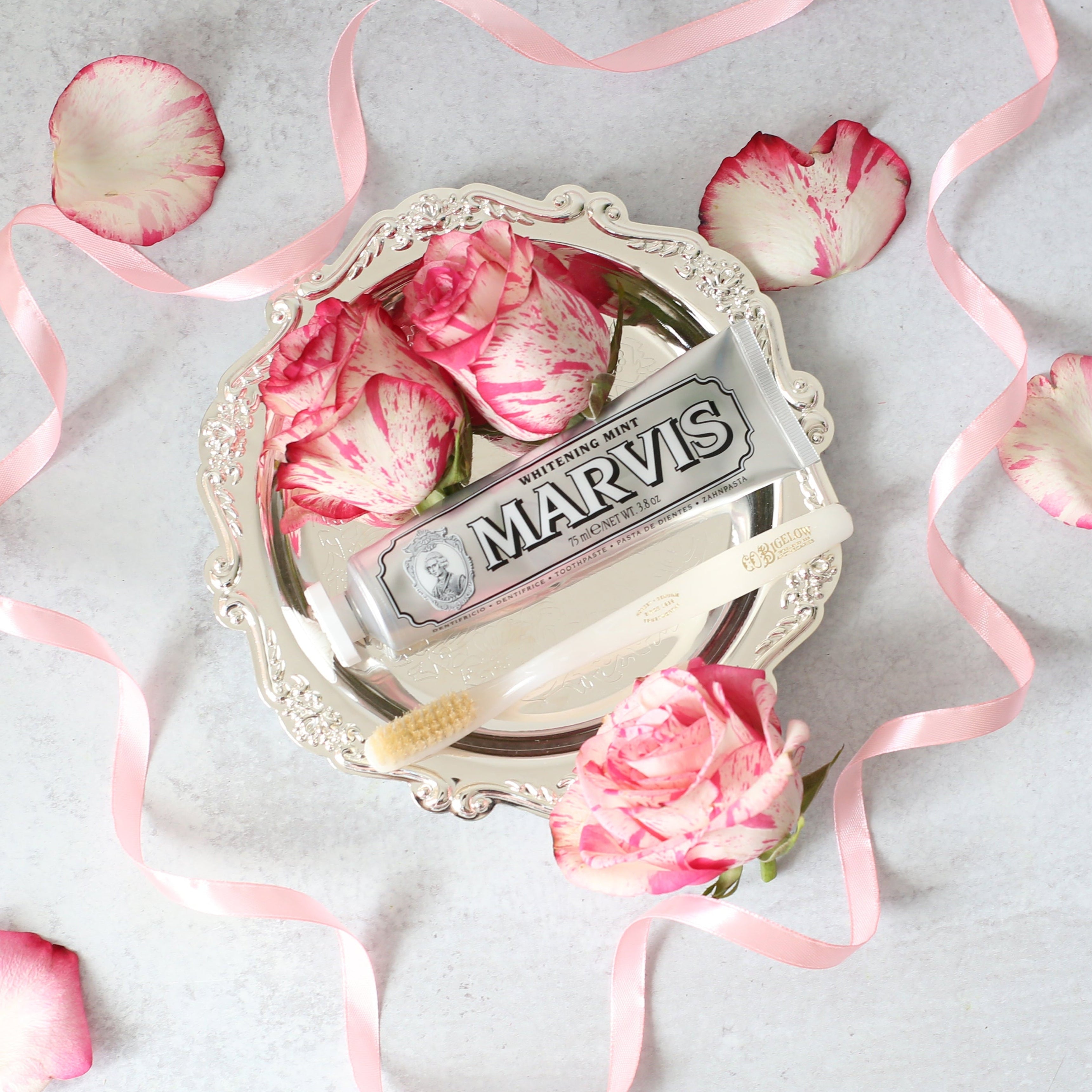 Silver decorative item with pink flowers and ribbons on a light gray background