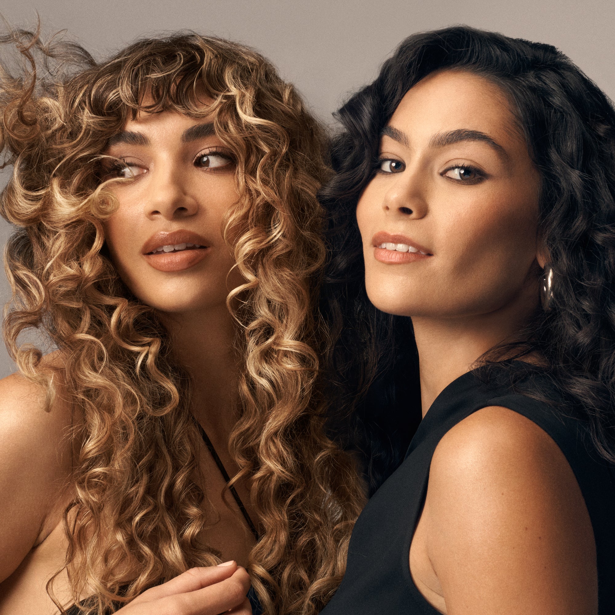 Two women with styled hair posing against a neutral background