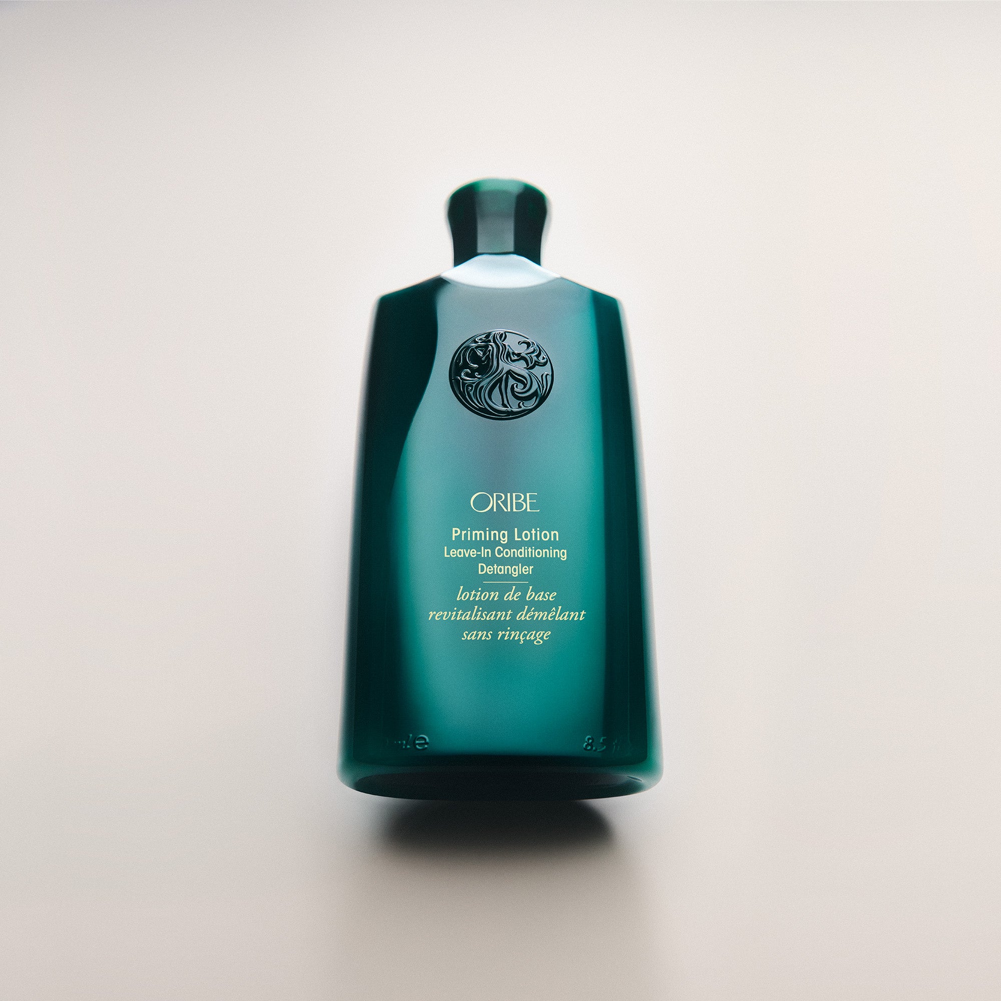 Green bottle of Oribe Priming Lotion on a light beige background