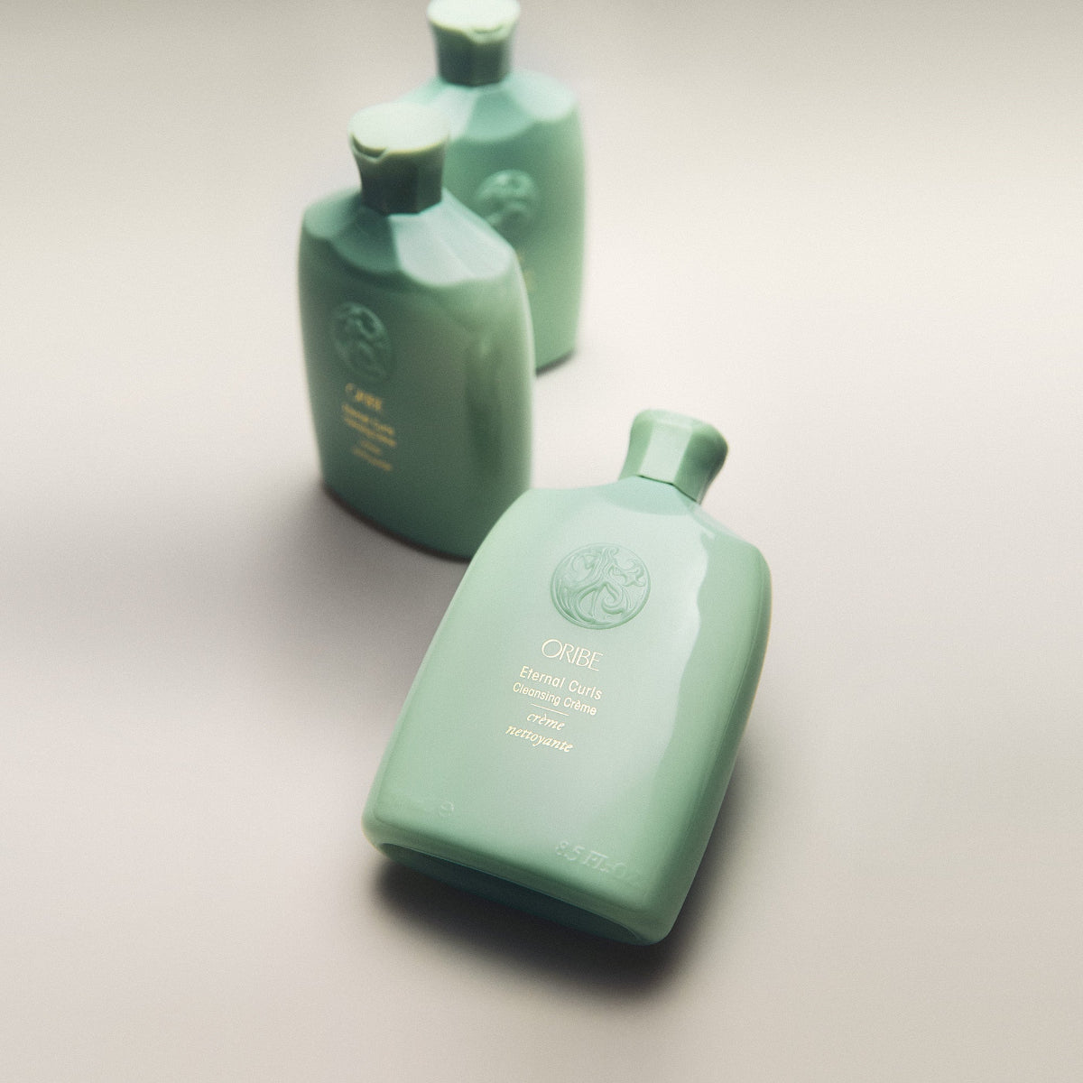 Three green bottles of Oribe hair product on a light gray background