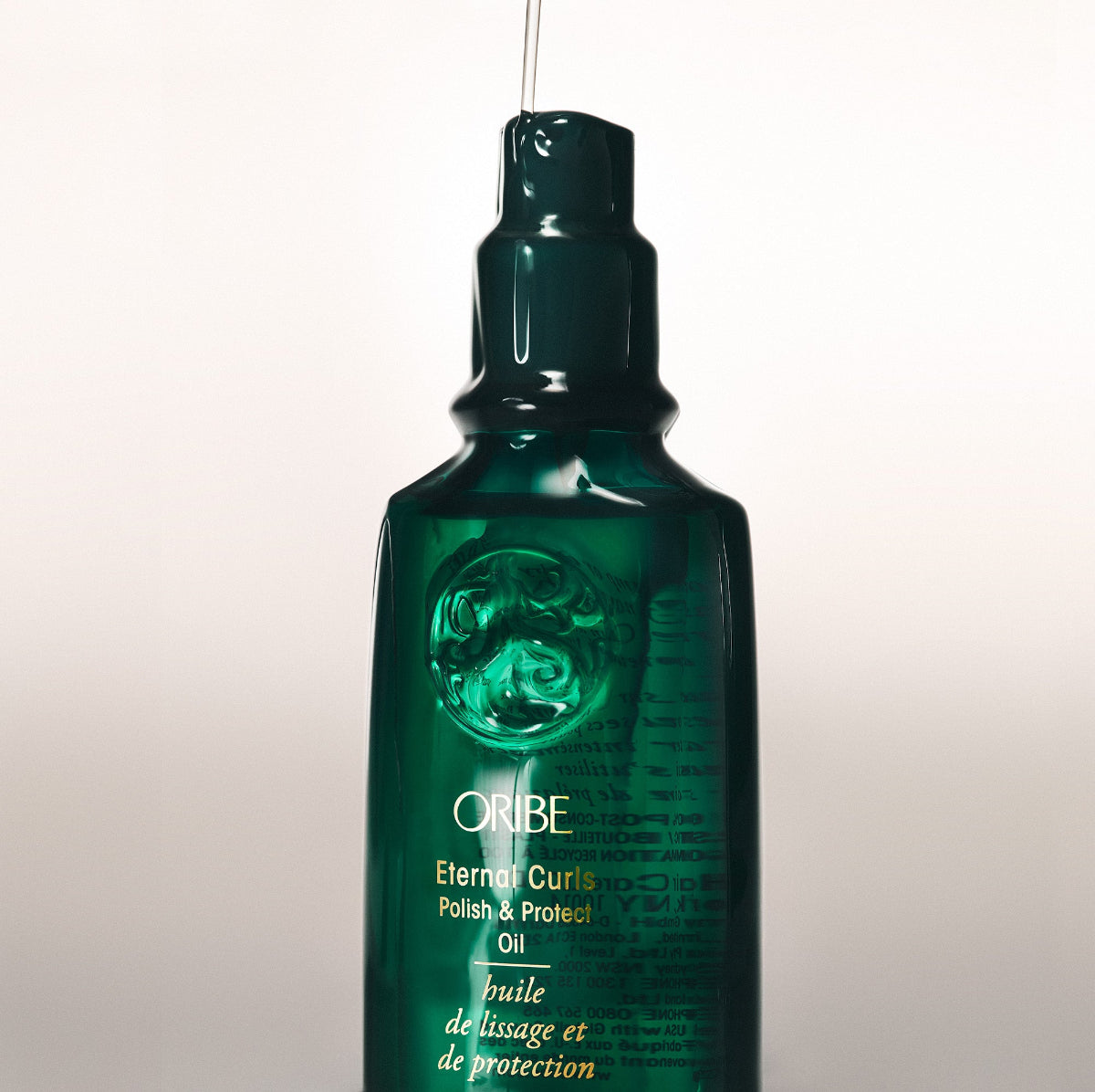 Green bottle of Oribe Eternal Curls Polish & Protect Oil on a light background