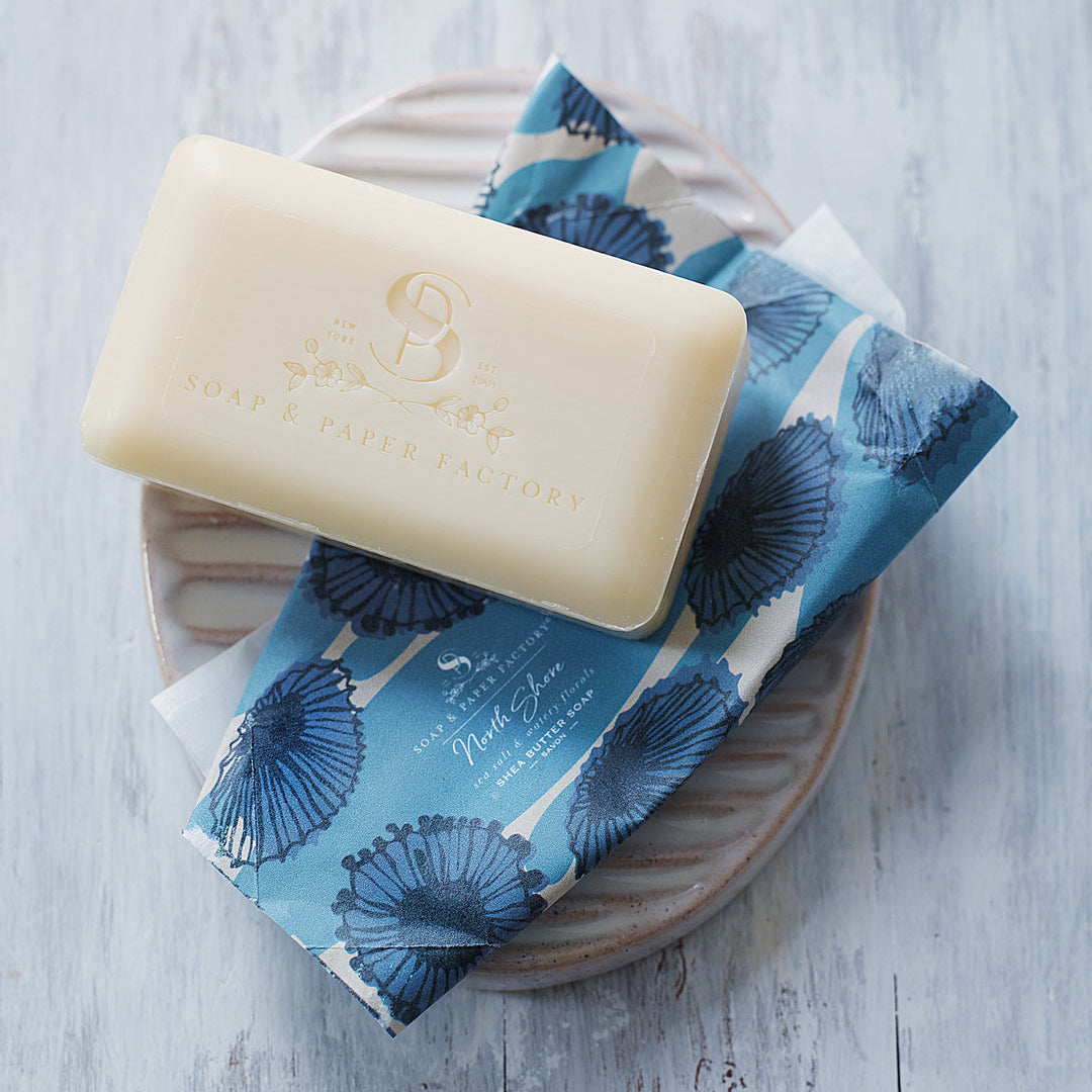 Bar of soap on a blue floral soap bag with a wooden tray on a light wooden surface