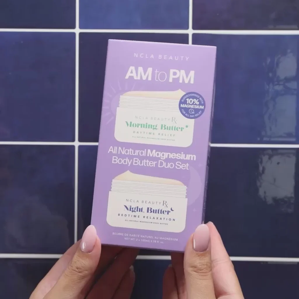 Hand holding a purple 'AM to PM' body butter set against a blue tiled wall.