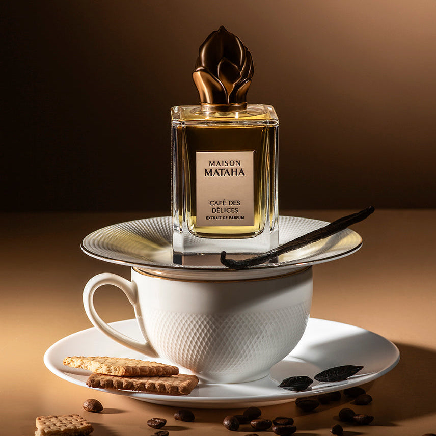 Perfume bottle on top of a coffee mug surrounded by biscuits and coffee beans