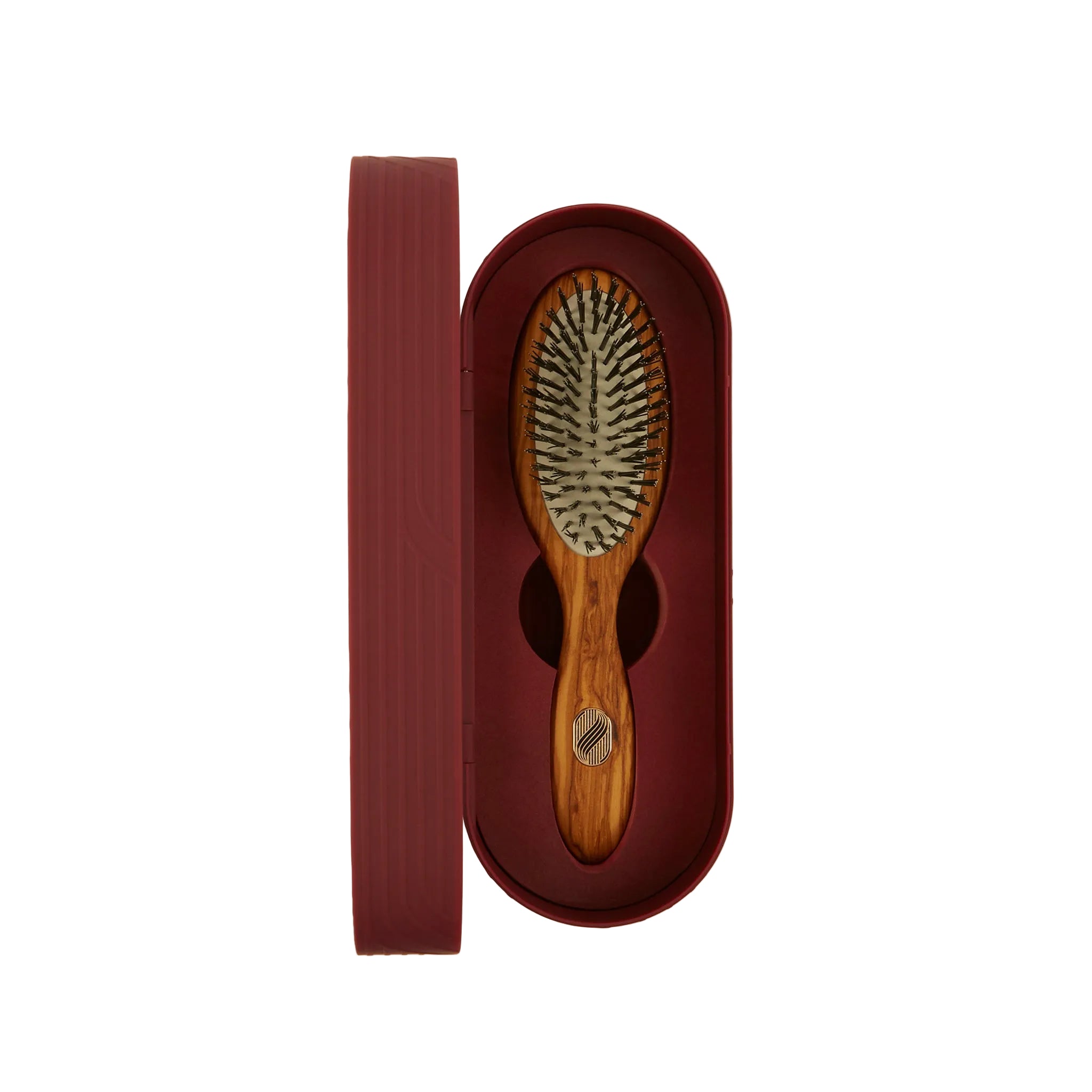 A wooden hairbrush with dark bristles presented in an open oval burgundy box next to its matching lid, on a light cream background.