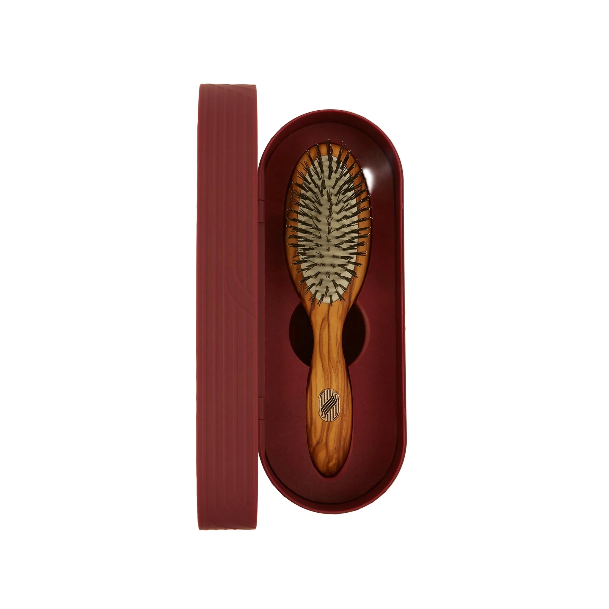 A wooden hairbrush with dark bristles, presented inside an open oval burgundy case next to its matching lid on a light cream background.