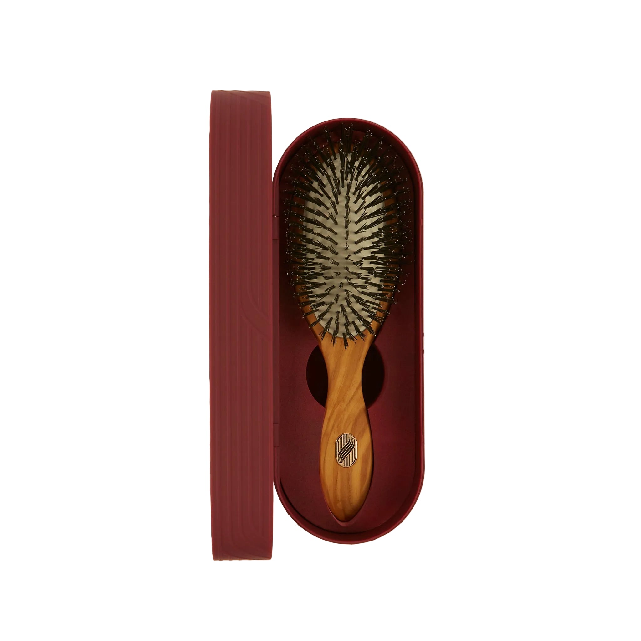 A wooden hairbrush with dark bristles resting inside an oval burgundy case, with the matching lid placed beside it on a clean off-white background.